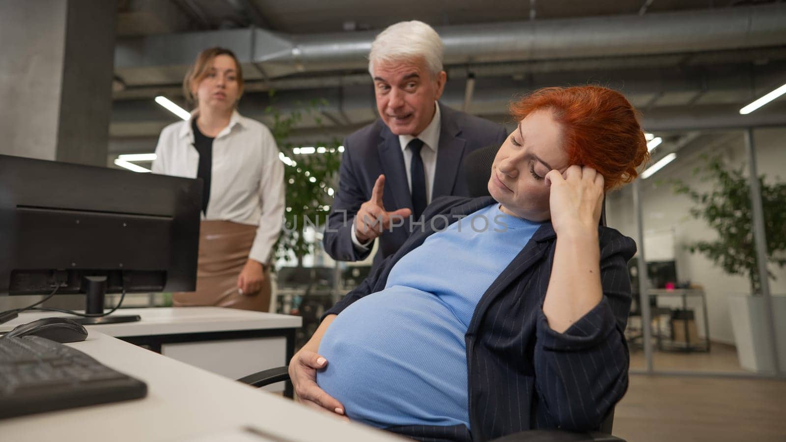 Elderly Caucasian man and woman giggling behind their sleeping pregnant colleague in the office. by mrwed54