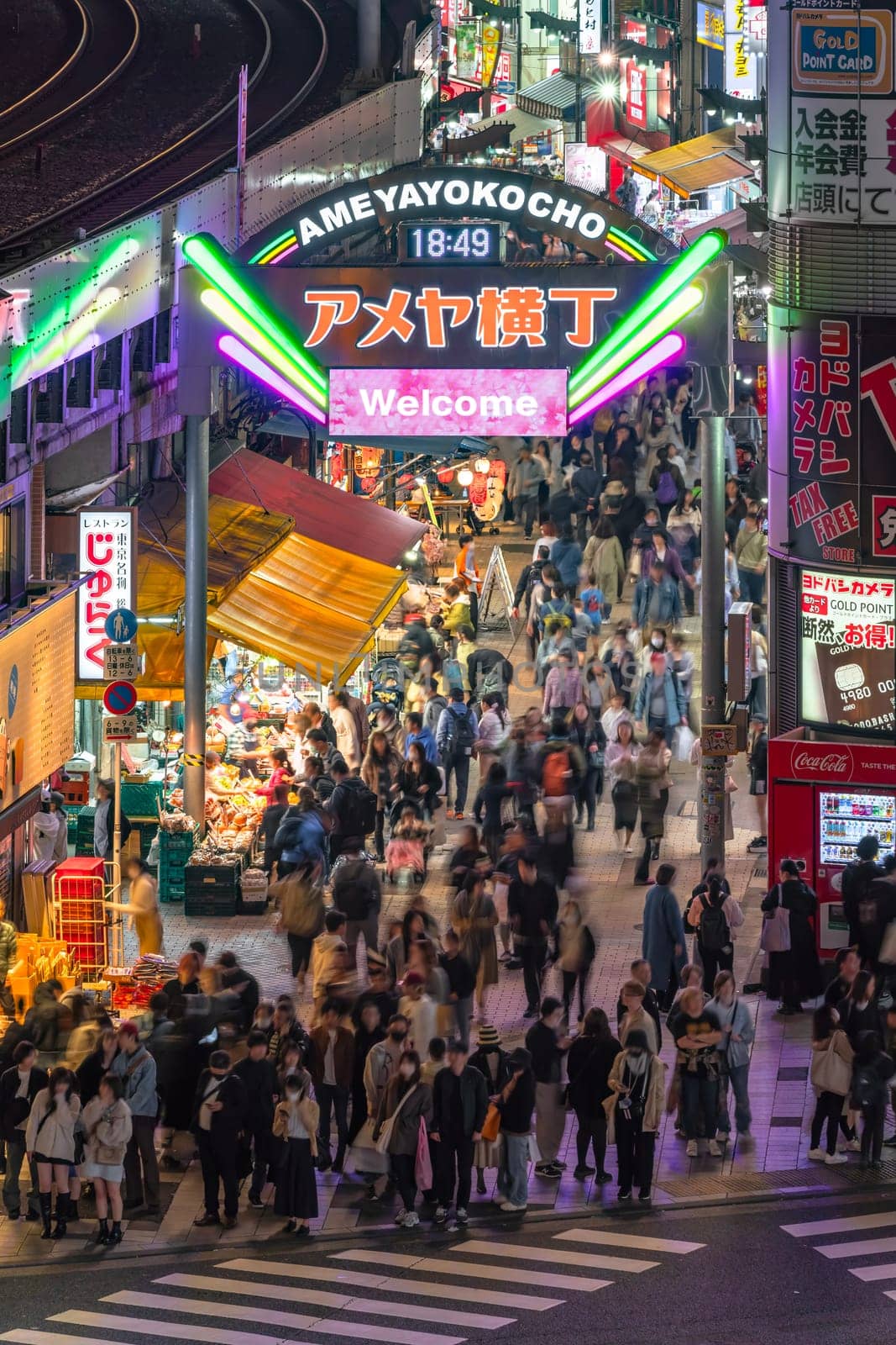 ueno, japan - apr 2 2024: Crowd of tourists waiting at night at foot of the illuminated Ameya Yokocho market street arch with a screen written in english 'Welcome' on a cherry blossoms background.