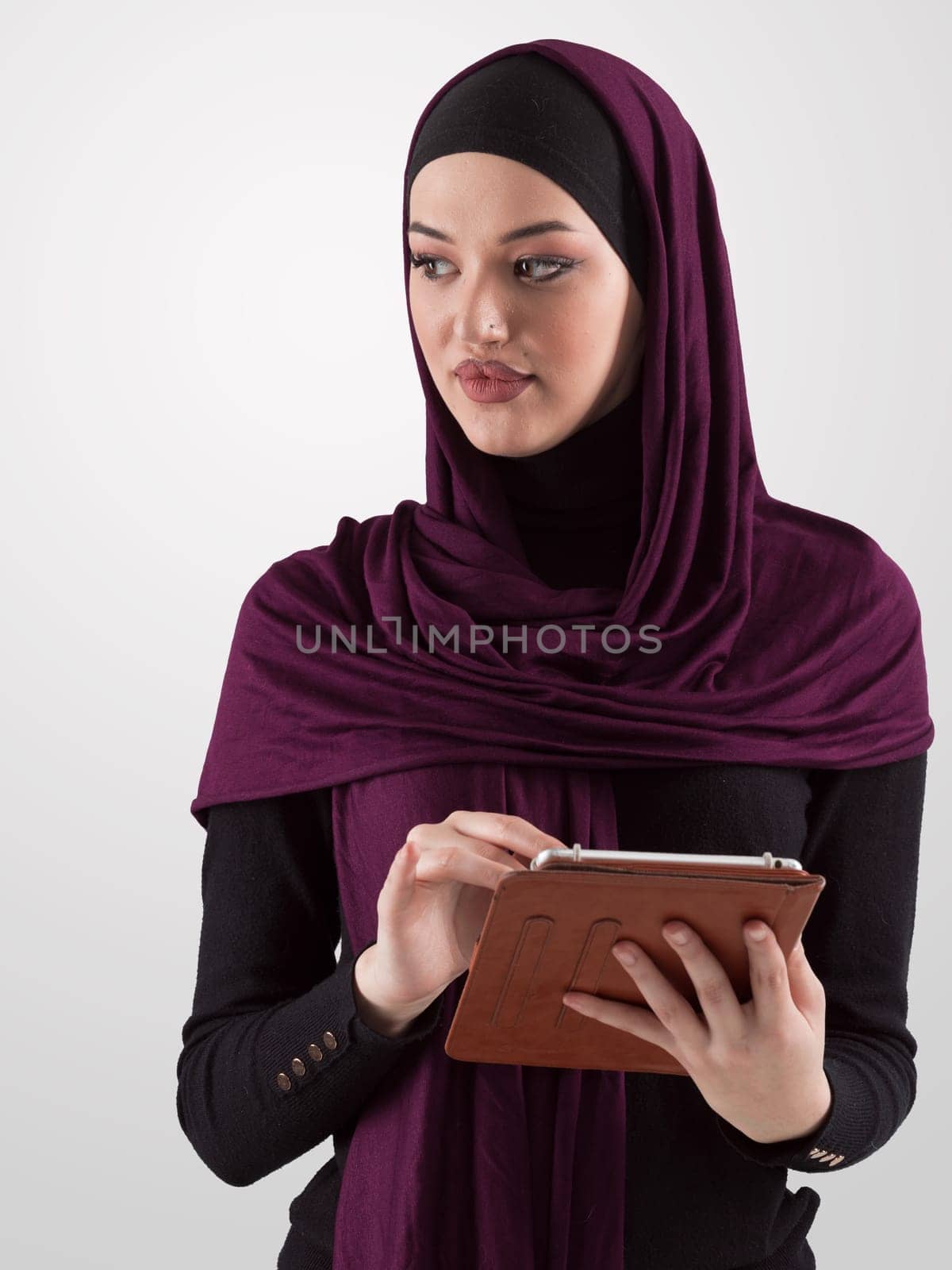 Beautiful and modern young Arabic businesswoman in hijab using a tablet computer while posing on light background and smiling at the camera. Business diversity concept, Muslim lady. High quality photo