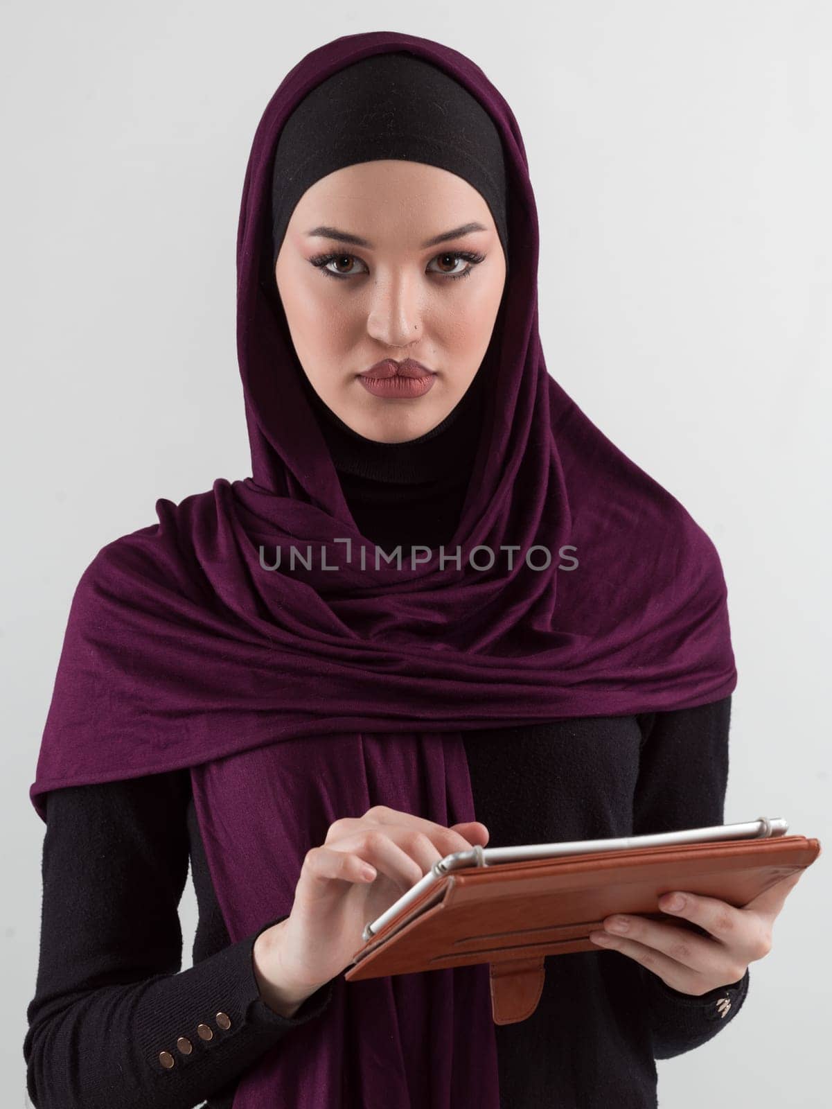 Beautiful and modern young Arabic businesswoman in hijab using a tablet computer while posing on light background and smiling at the camera. Business diversity concept, Muslim lady. by dotshock