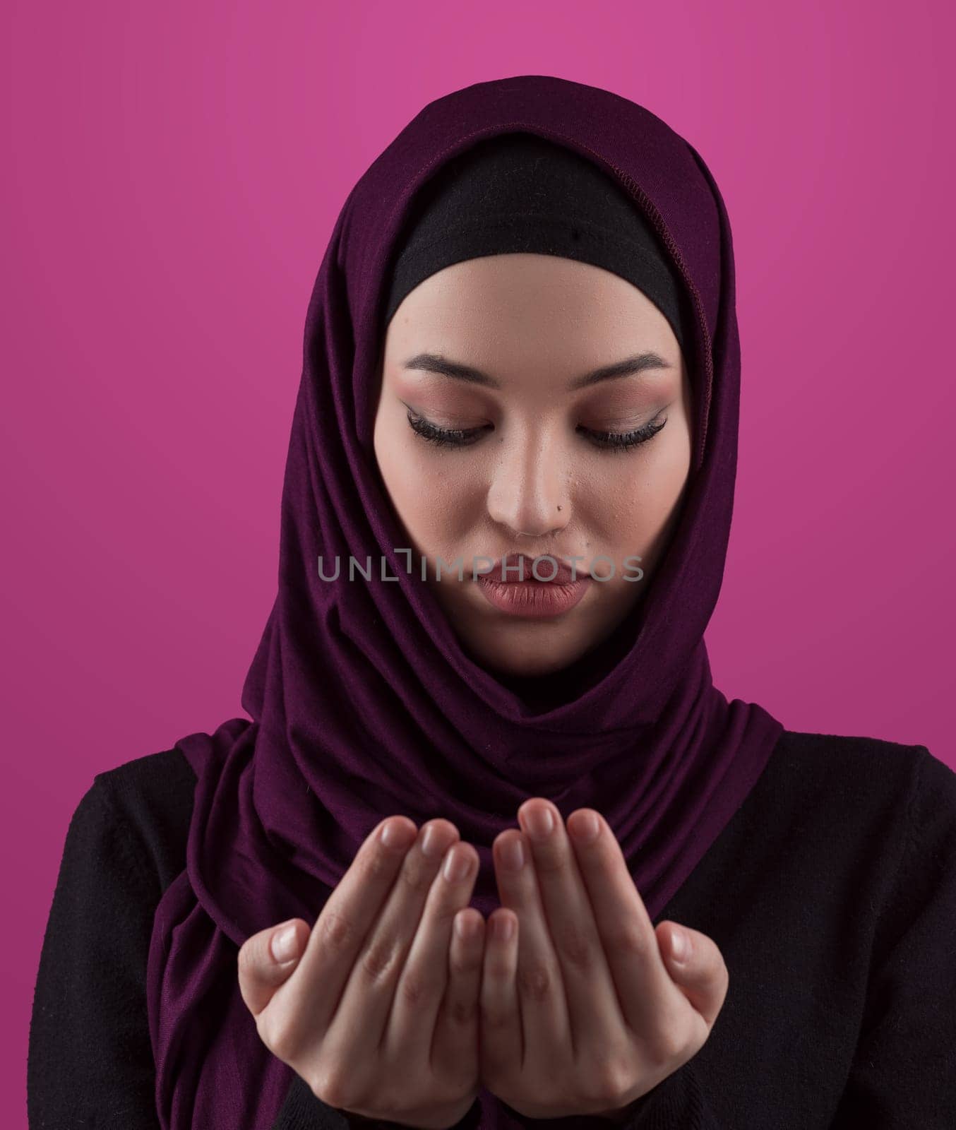 Muslim woman in hijab and traditional clothes praying for Allah, copy space. Muslim woman with hijab praying indoor pink background. High quality photo