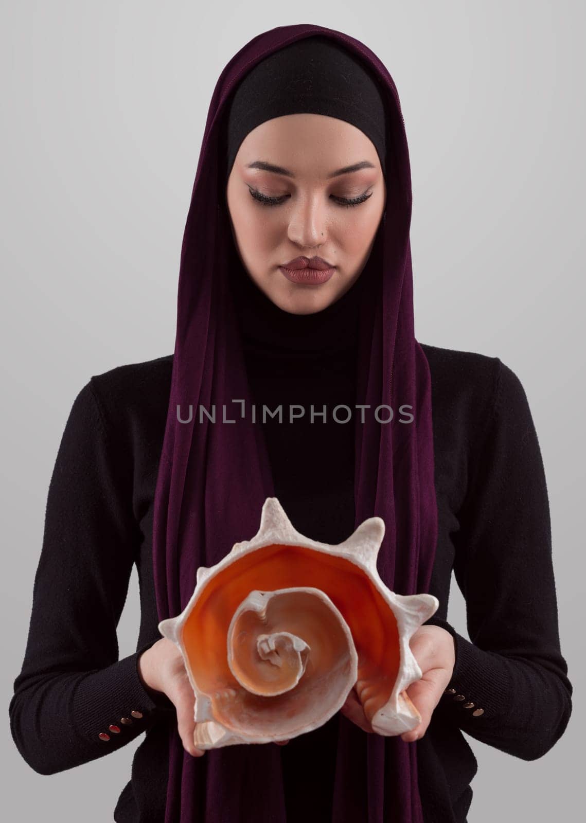 Pretty stylish Muslim woman wearing hijab and holding a seashell and dreams closed eyes. Golden ratio and ideal proportion concept. by dotshock