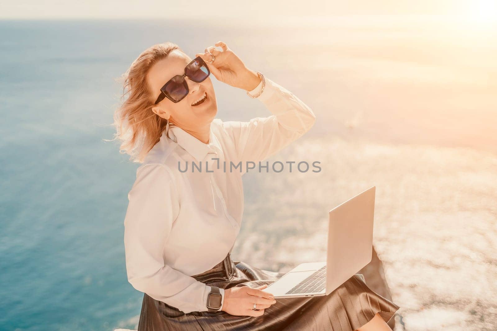 Business woman on nature in white shirt and black skirt. She works with an iPad in the open air with a beautiful view of the sea. The concept of remote work