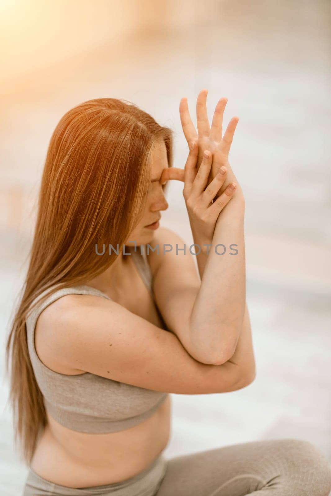 Young woman doing yoga in the gym. A girl with long hair and in a beige tracksuit stands in a cow pose on a pink carpet. A woman performs Gomukhasana