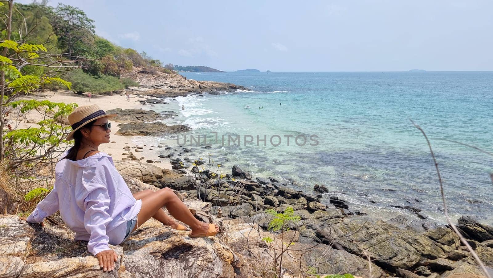 Koh Samet Island Thailand, Asian Thai women sitting on a rock looking out over the bay with a tropical beach and a blue ocean