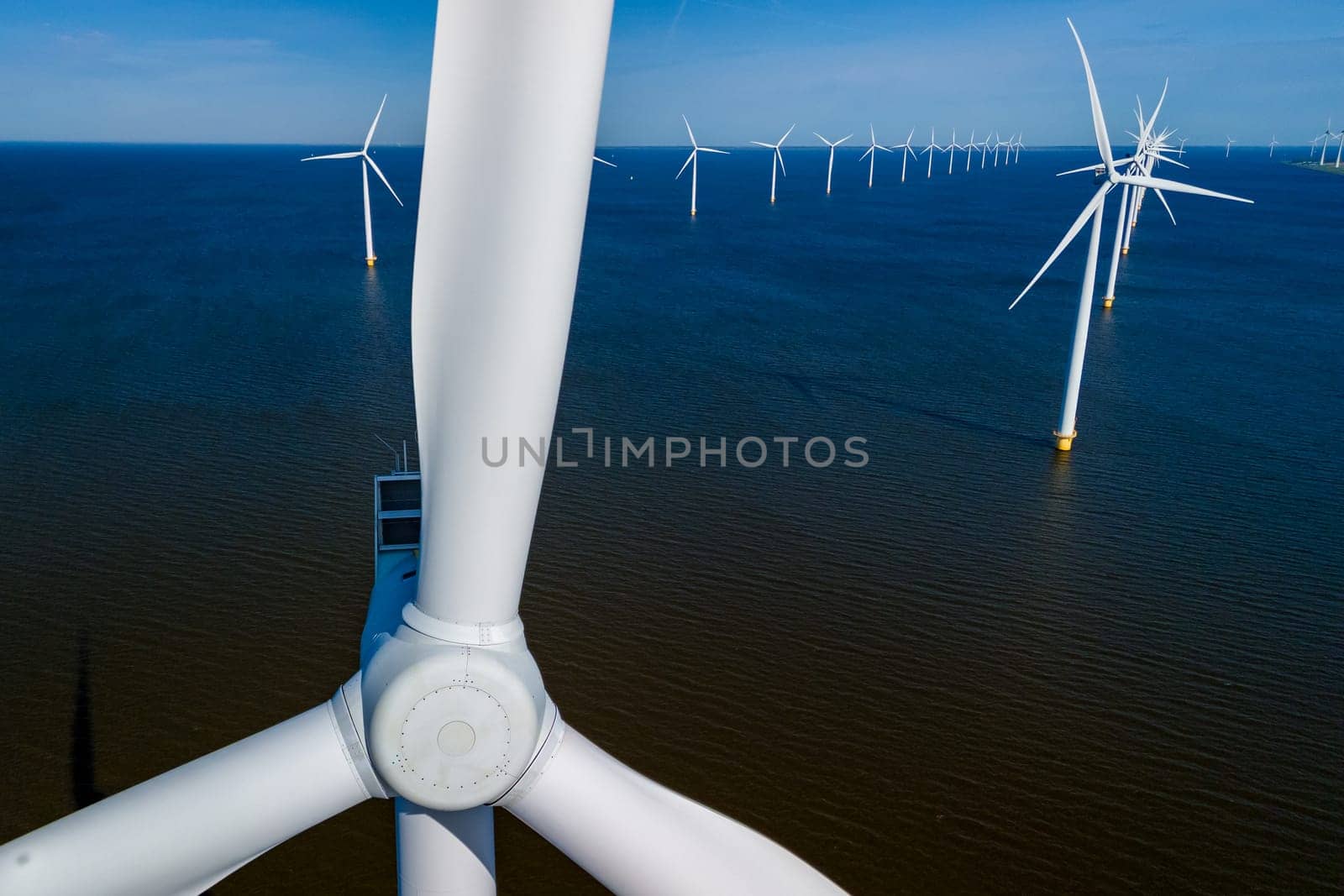 Beams of sunshine illuminate a vast wind farm in the ocean, showcasing rows of elegant windmill turbines standing tall in the Netherlands Flevoland during the vibrant season of Spring.