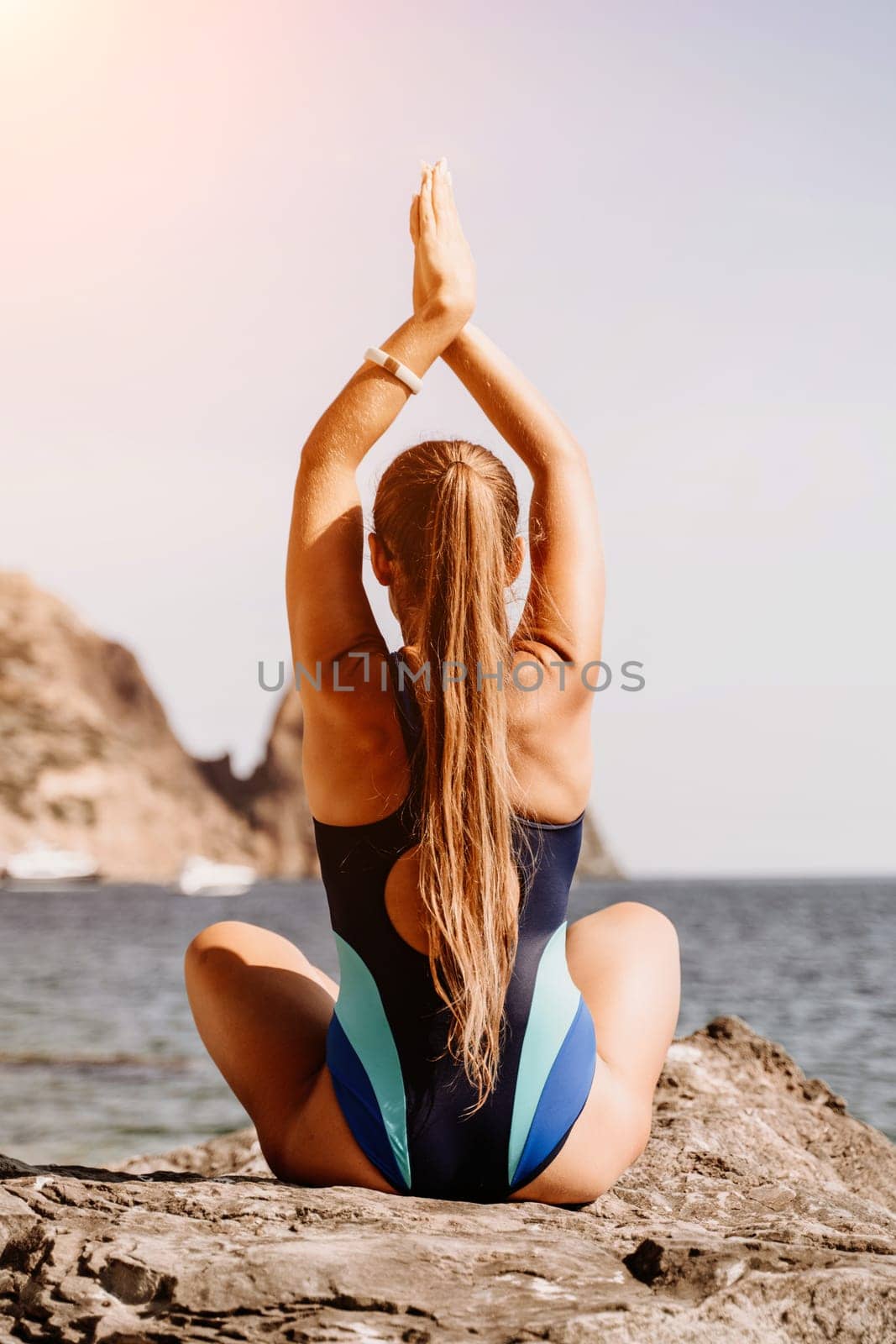 Yoga on the beach. A happy woman meditating in a yoga pose on the beach, surrounded by the ocean and rock mountains, promoting a healthy lifestyle outdoors in nature, and inspiring fitness concept