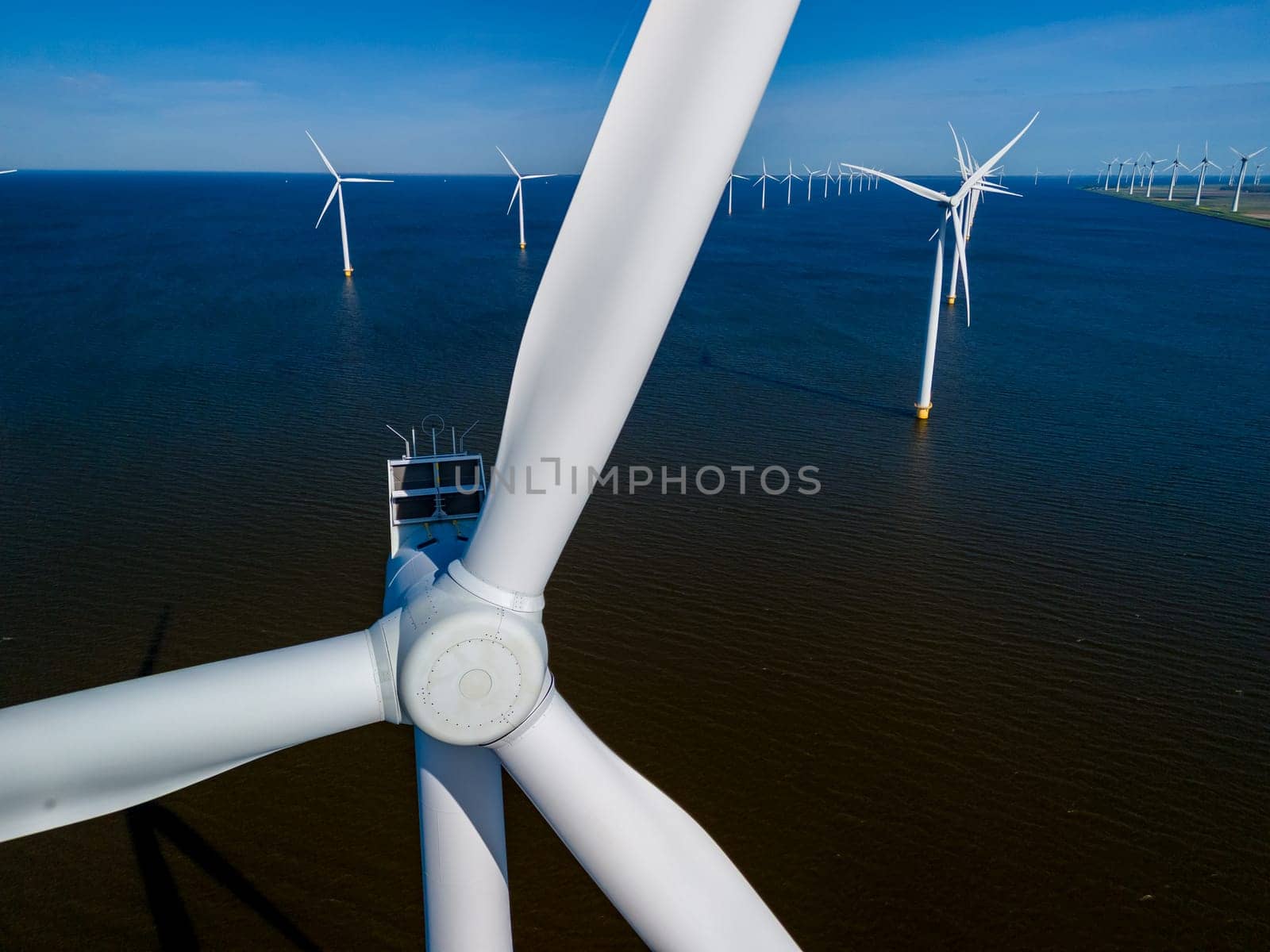 A stunning sight unfolds as windmill turbines gracefully harvest energy from the wind in the middle of a vast body of water in the Netherlands Flevoland region during the vibrant season of Spring.