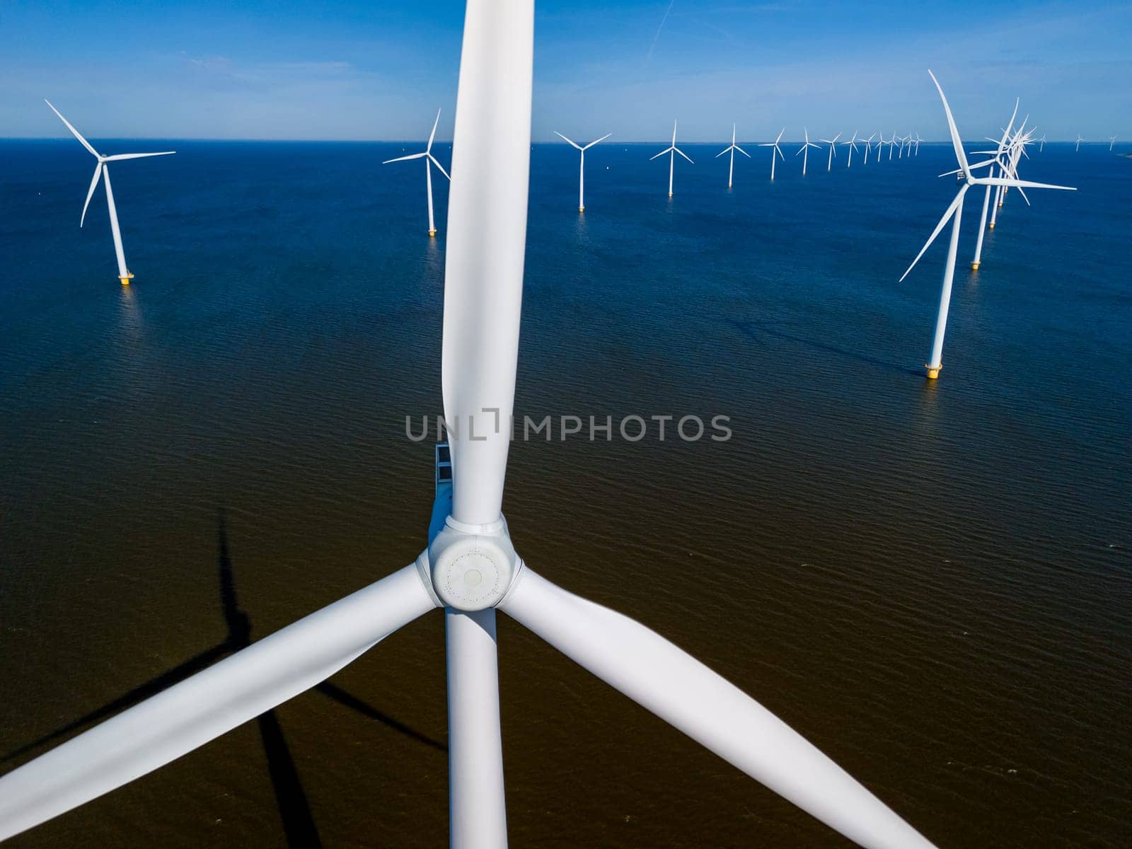 A cluster of towering wind turbines stands tall in the ocean in the spring breeze by fokkebok