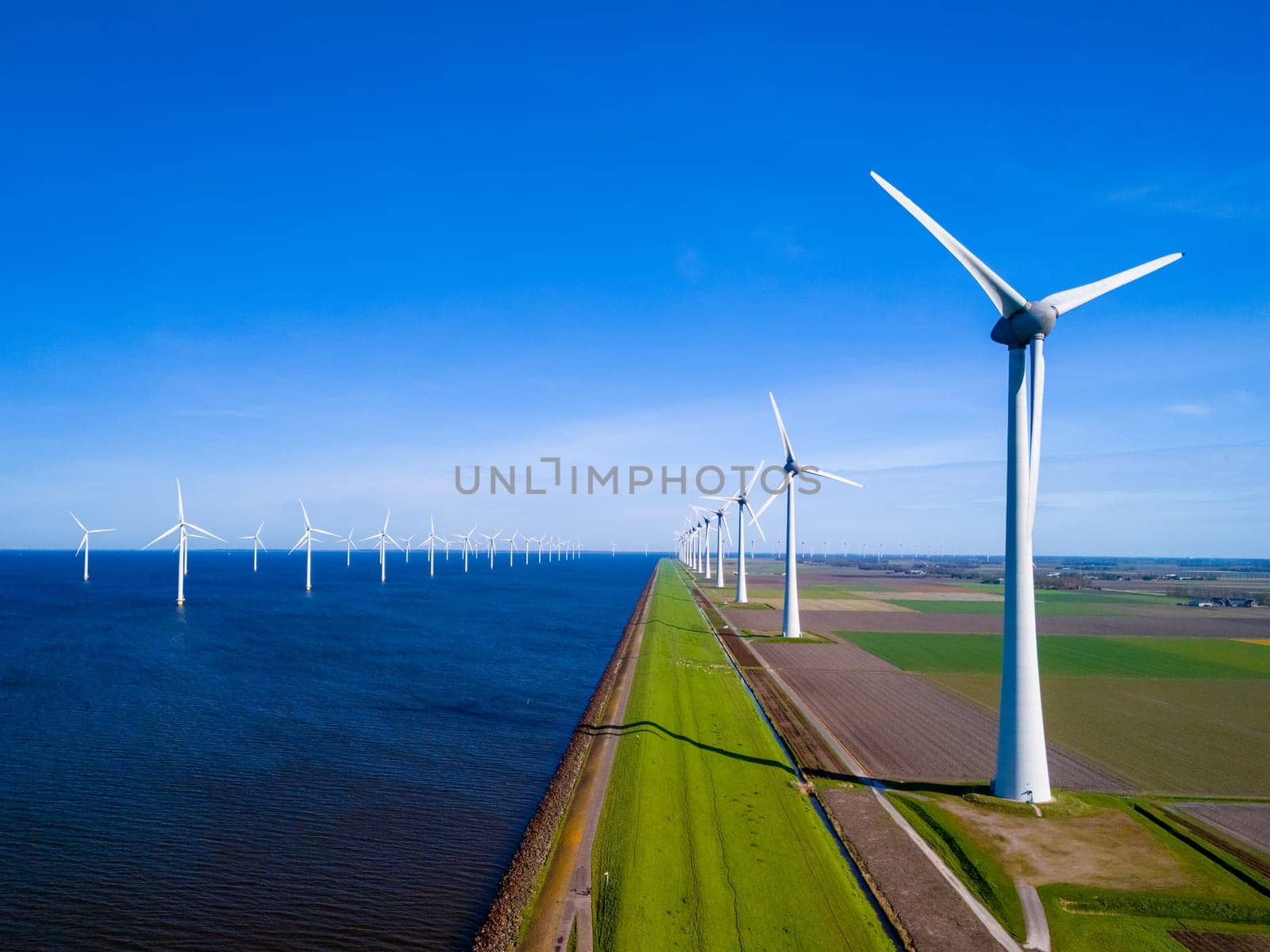 A serene scene of a row of wind turbines standing tall next to a calm body of water ocean by fokkebok