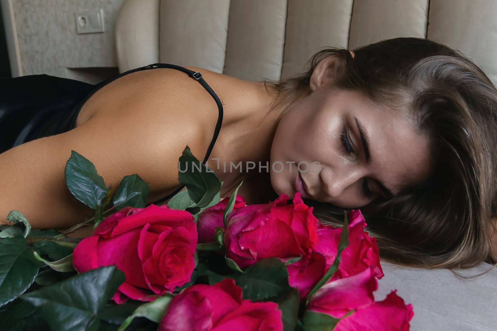 A woman lays on a bed with a bouquet of red roses in her lap. Concept of romance and intimacy, as the woman is surrounded by the flowers and he is in a vulnerable position