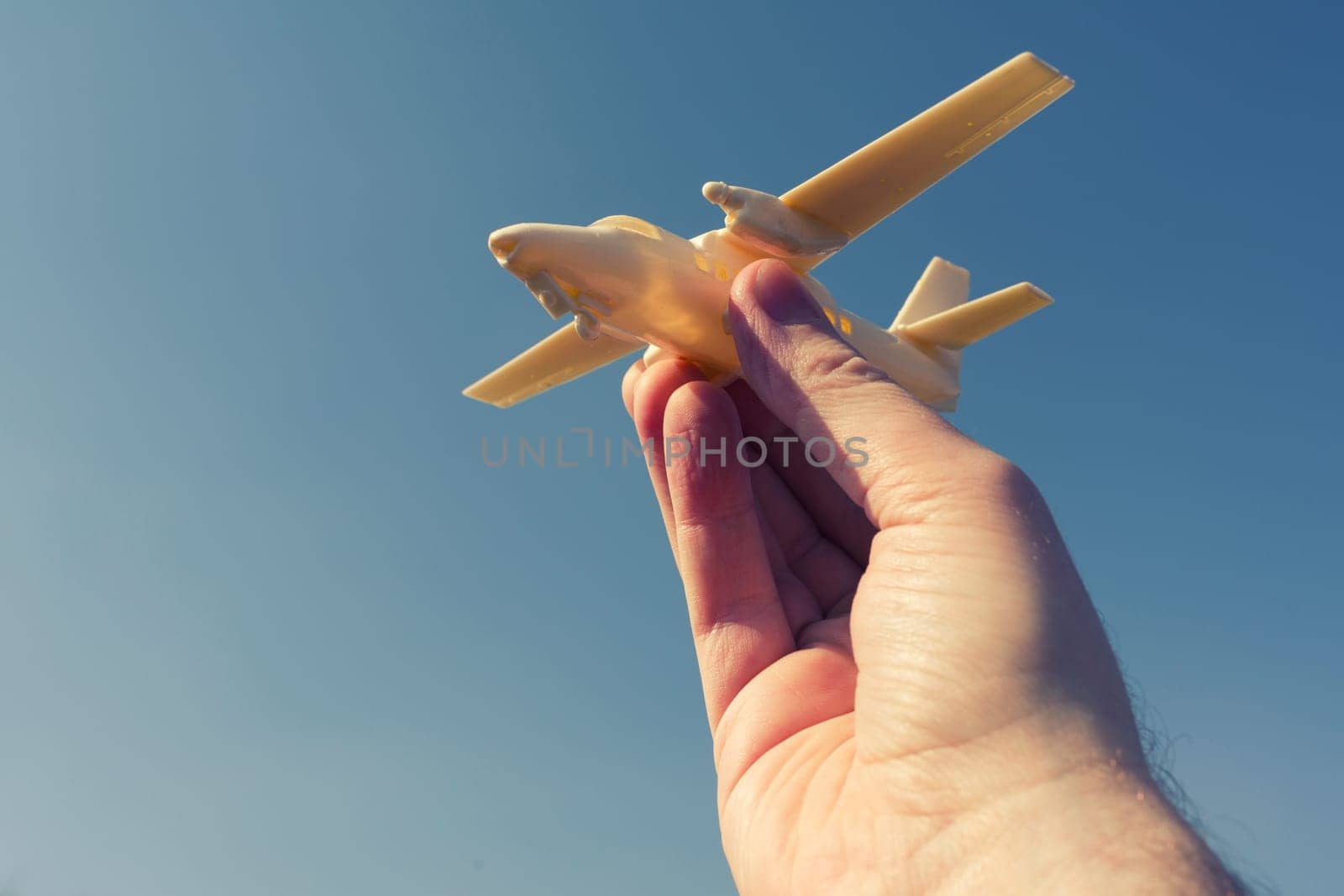 close up photo of male hand holding toy airplane against blue sky. by zartarn