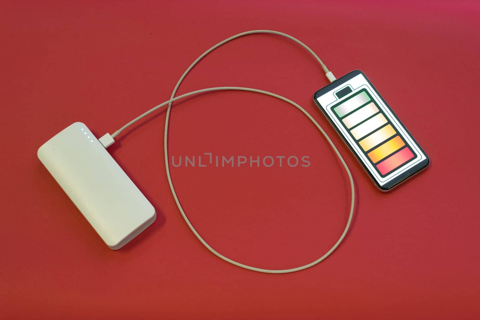 Smartphone is charging with power bank on red background - image