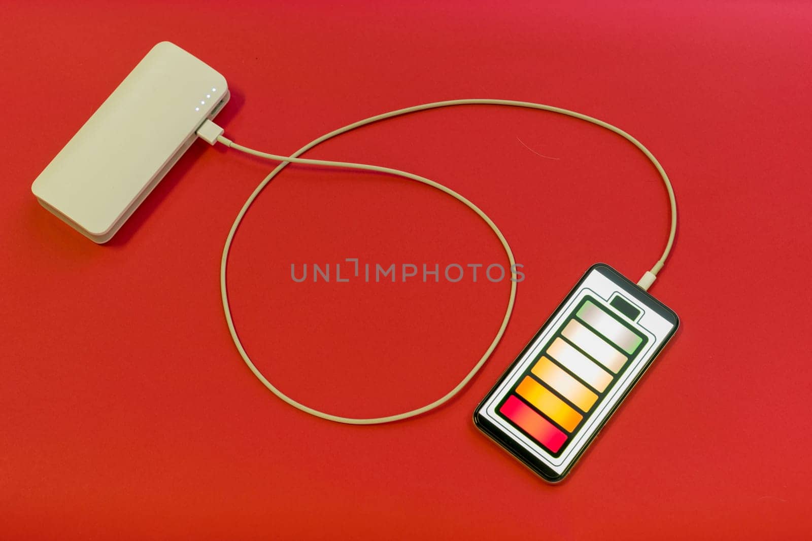 Smartphone is charging with power bank on red background - image
