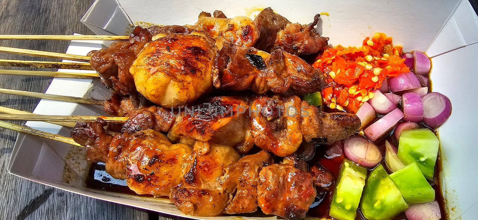 Lamb grilled satay served with barbecue savory sauce and pickled onion, chili and cucumber, selective focus photo on top of wooden table