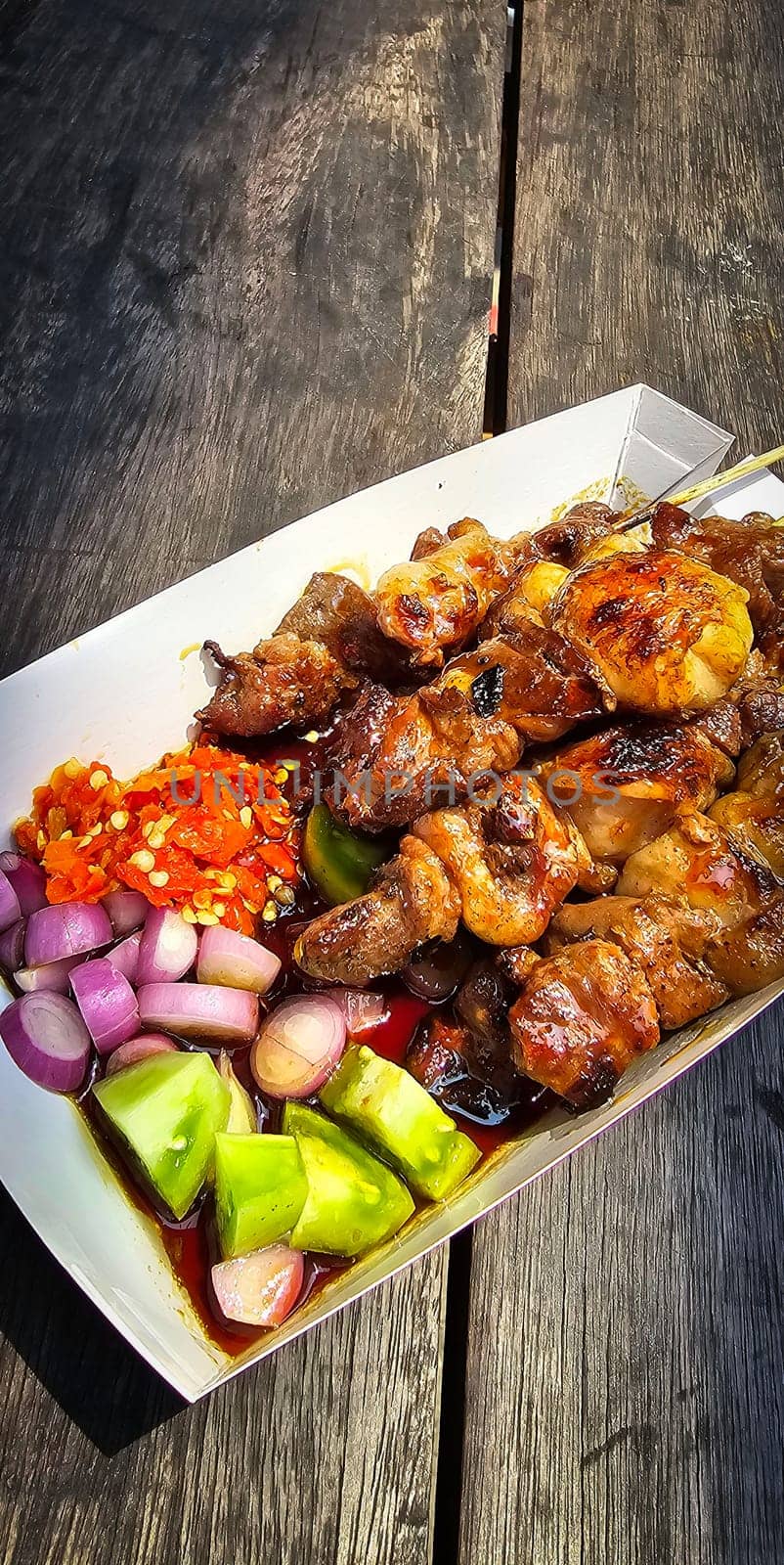 Lamb grilled satay served with barbecue savory sauce and pickled onion, chili and cucumber, selective focus photo on top of wooden table