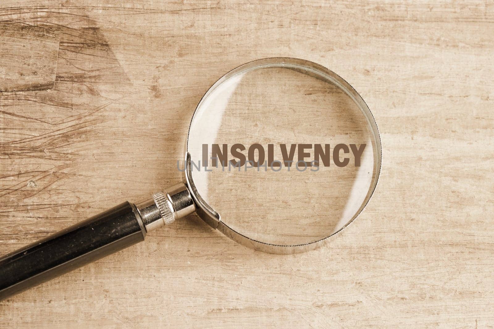 Debt relief concept. A word INSOLVENCY visible through a magnifying glass on an old faded background