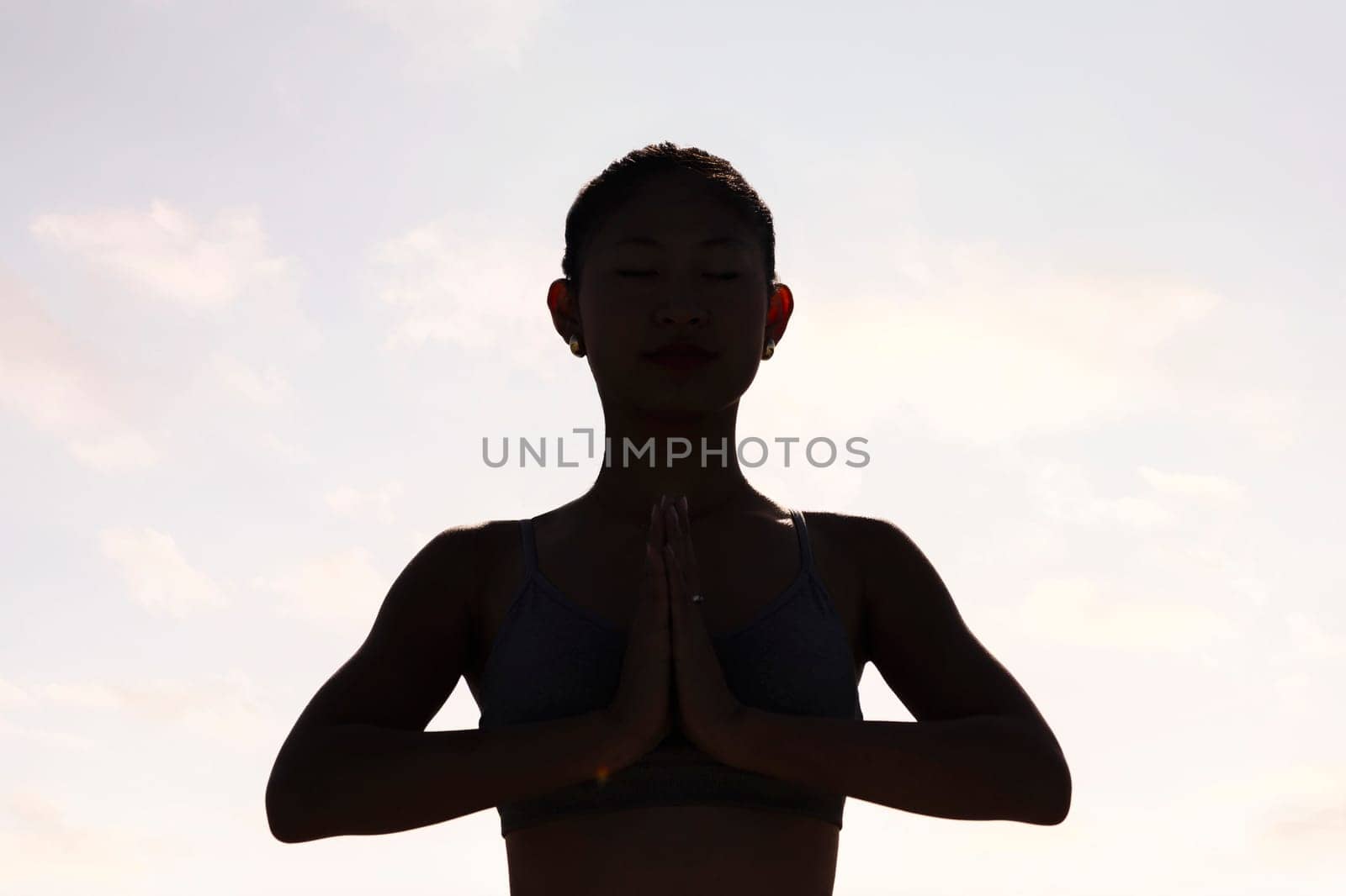 backlight portrait of young woman practicing yoga in pray position, concept of mental relaxation and healthy lifestyle, copy space for text