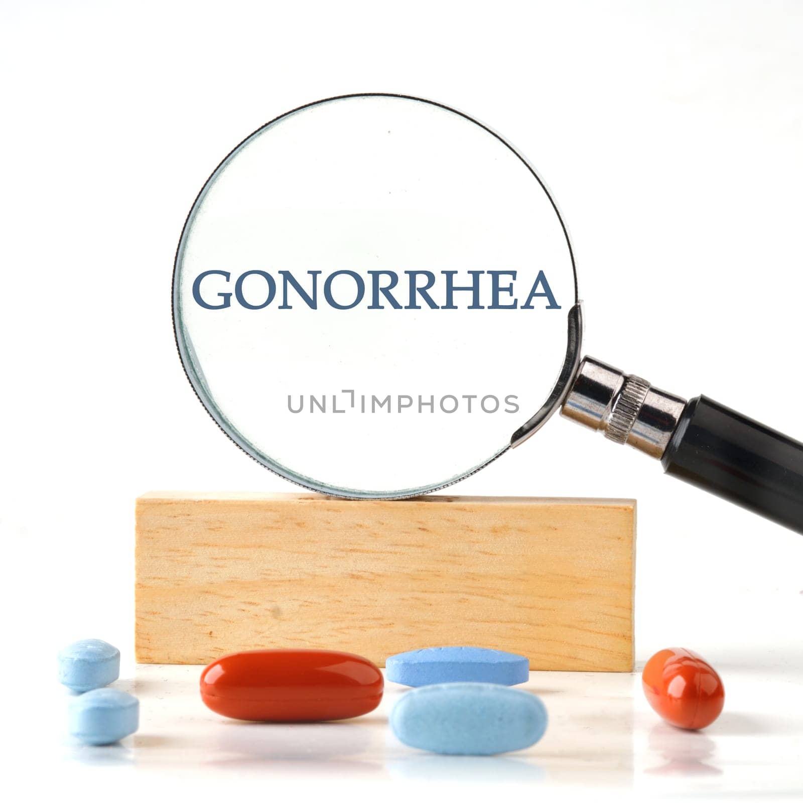 GONORRHEA word through a magnifying glass on a wooden block with vitamins, pills in the foreground