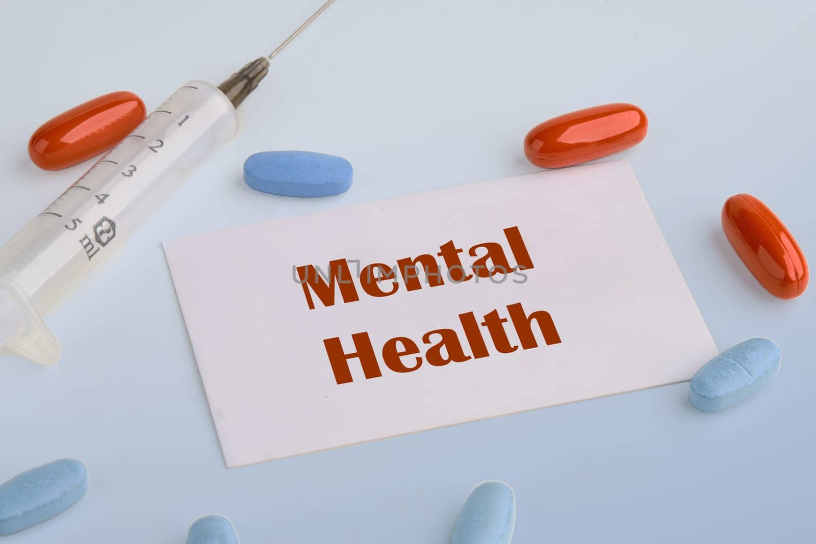 Health concept. Mental Health text on a white business card on a blue background next to a syringe, pills, vitamins