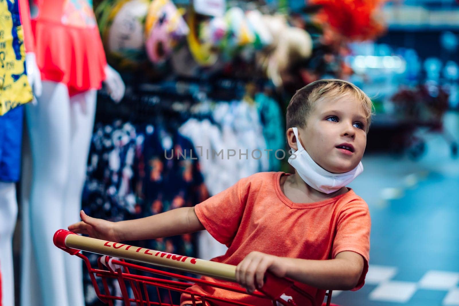 Boy sitting in shopping cart clothing store hypermarket, interested curious emotion, happy childhood.