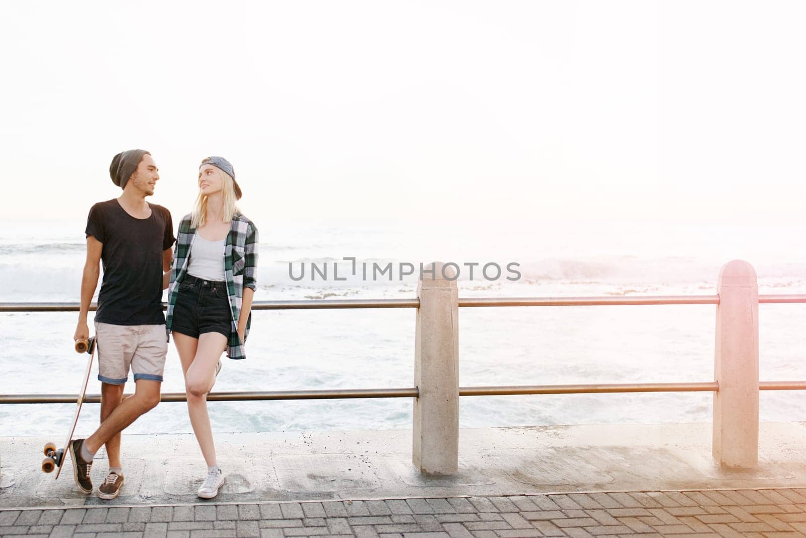 Couple, love and happy with skateboard at beach in summer or hot weather, together with sunset in London. Relationship, commitment and bonding for romance with soulmate, care and smile in boardwalk by YuriArcurs