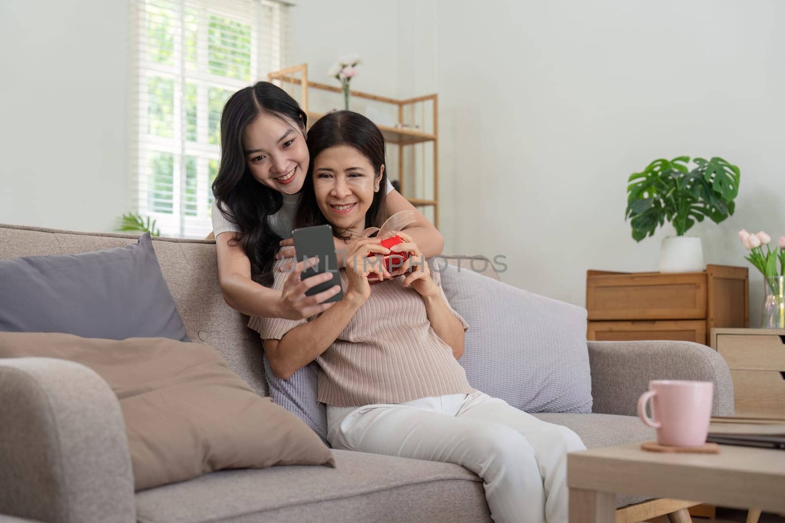 Daughter adult taking selfie using mobile phone with senior mother at home.