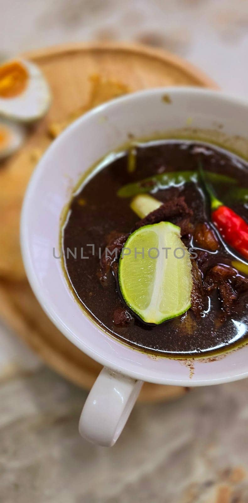 Rawon or Indonesian black beef soup, black color are from indonesian nut called kluwek. Served with lime, chili paste, salted egg, and tempe cracker. Perfect for recipe, article, or any cooking contents or blog