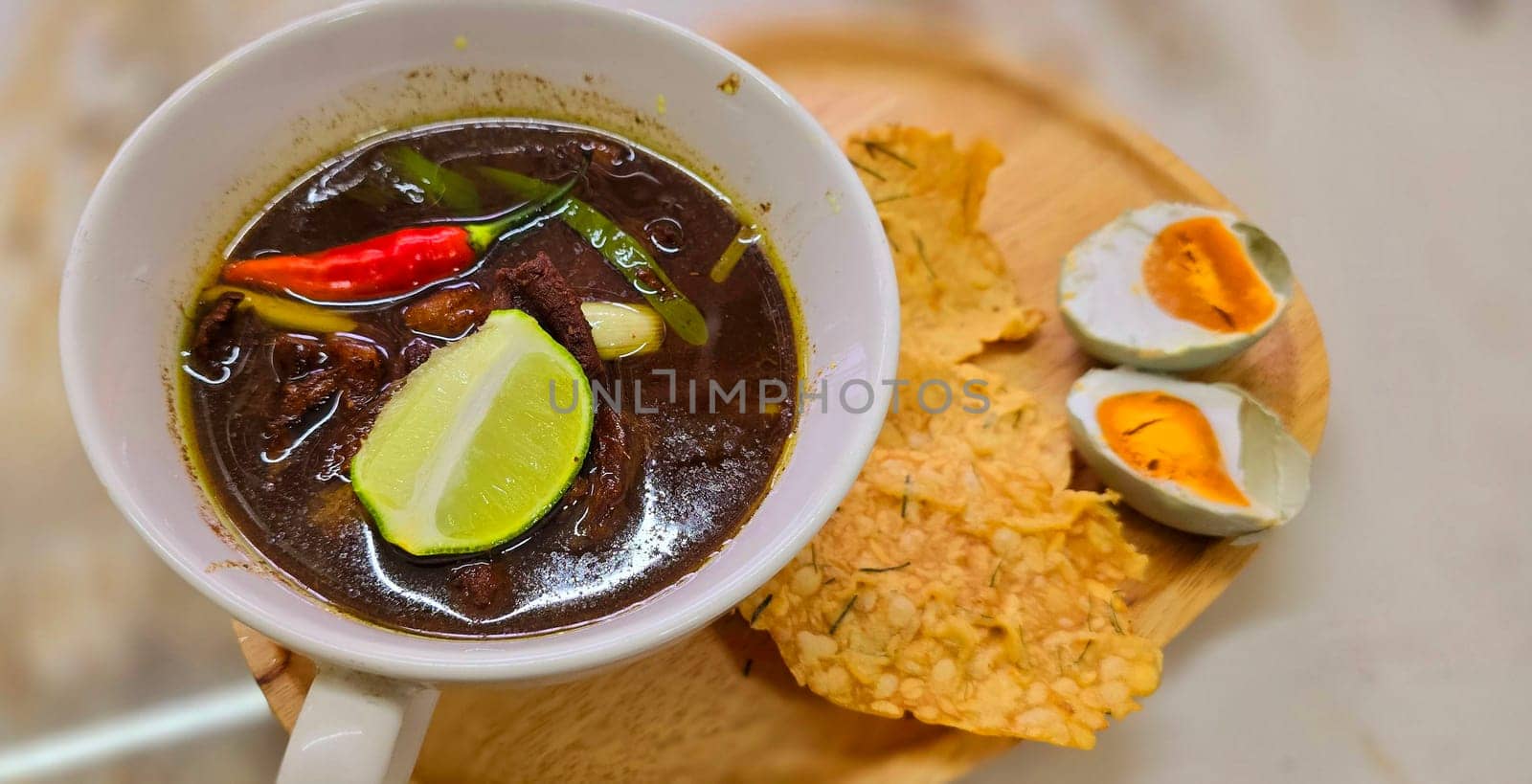 Rawon or Indonesian black beef soup, black color are from indonesian nut called kluwek. Served with lime, chili paste, salted egg, and tempe cracker. Perfect for recipe, article, or any cooking contents or blog