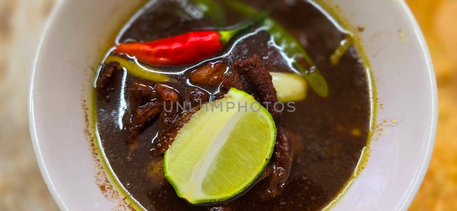 Rawon or Indonesian black beef soup, black color are from indonesian nut called kluwek. Served with lime, chili paste, salted egg, and tempe cracker. Perfect for recipe, article, or any cooking contents or blog