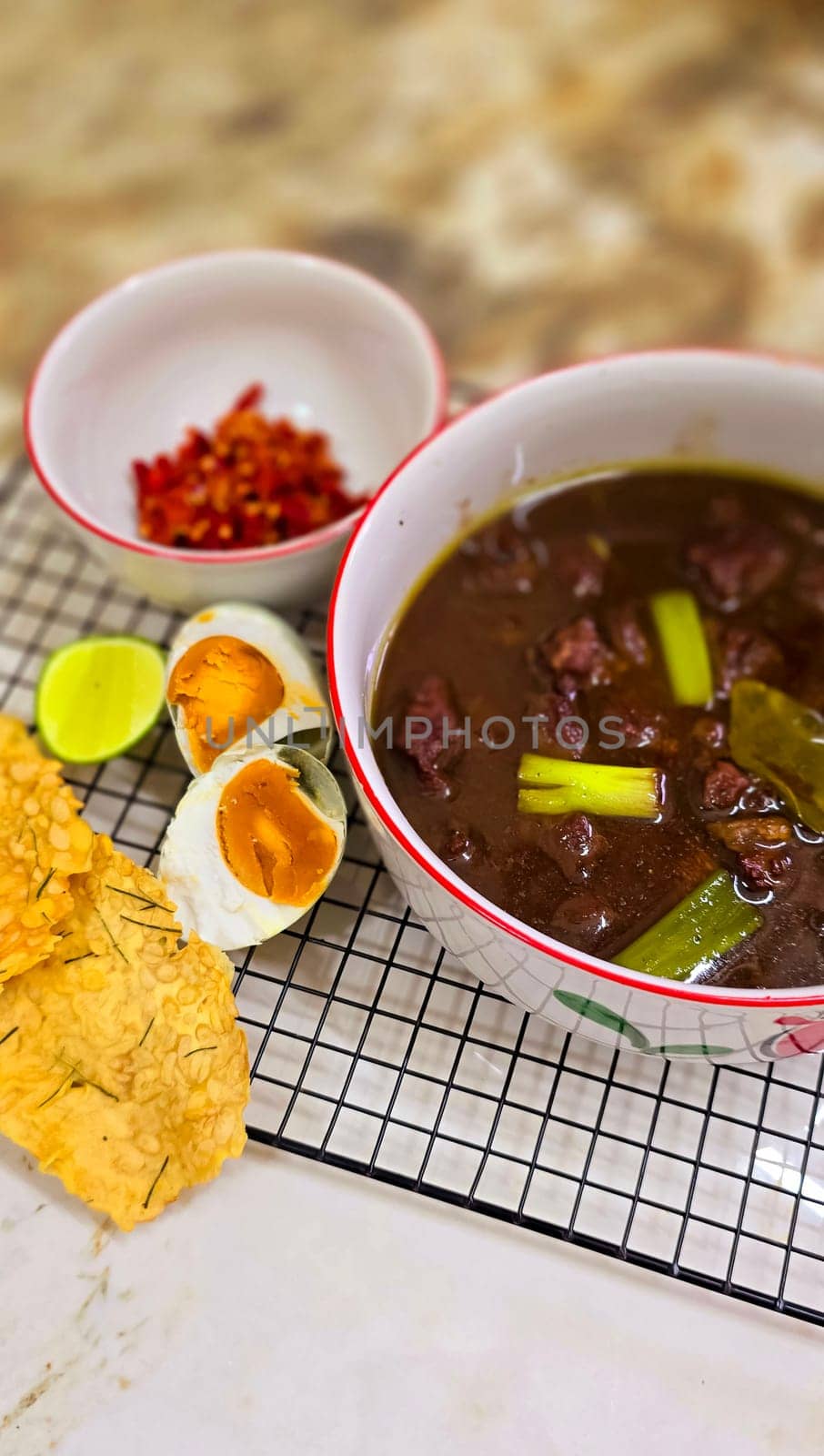 Rawon or Indonesian black beef soup, black color are from indonesian nut called kluwek. Served with lime, chili paste, salted egg, and tempe cracker. Perfect for recipe, article, or any cooking contents or blog