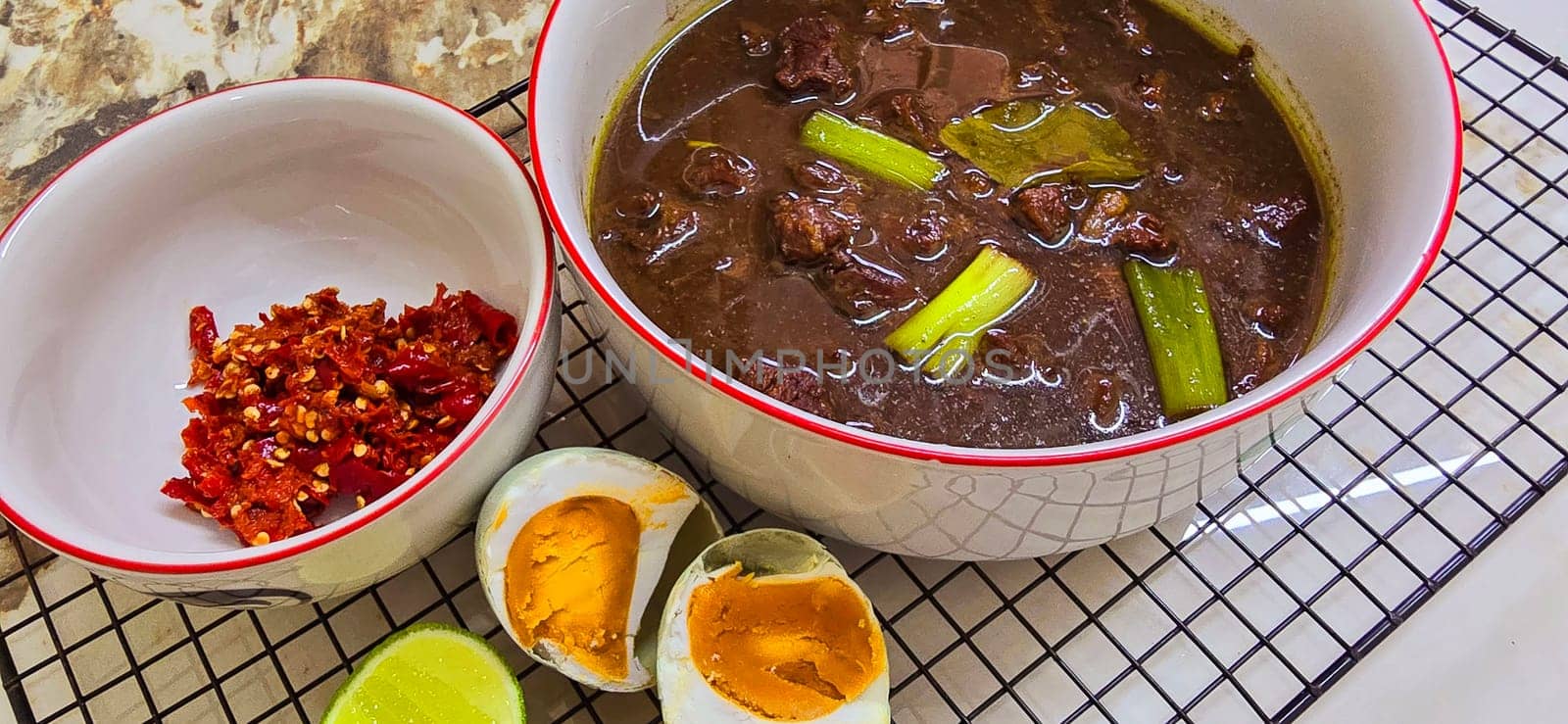 Rawon or Indonesian black beef soup, black color are from indonesian nut called kluwek. Served with lime, chili paste, salted egg, and tempe cracker. Perfect for recipe, article, or any cooking contents or blog