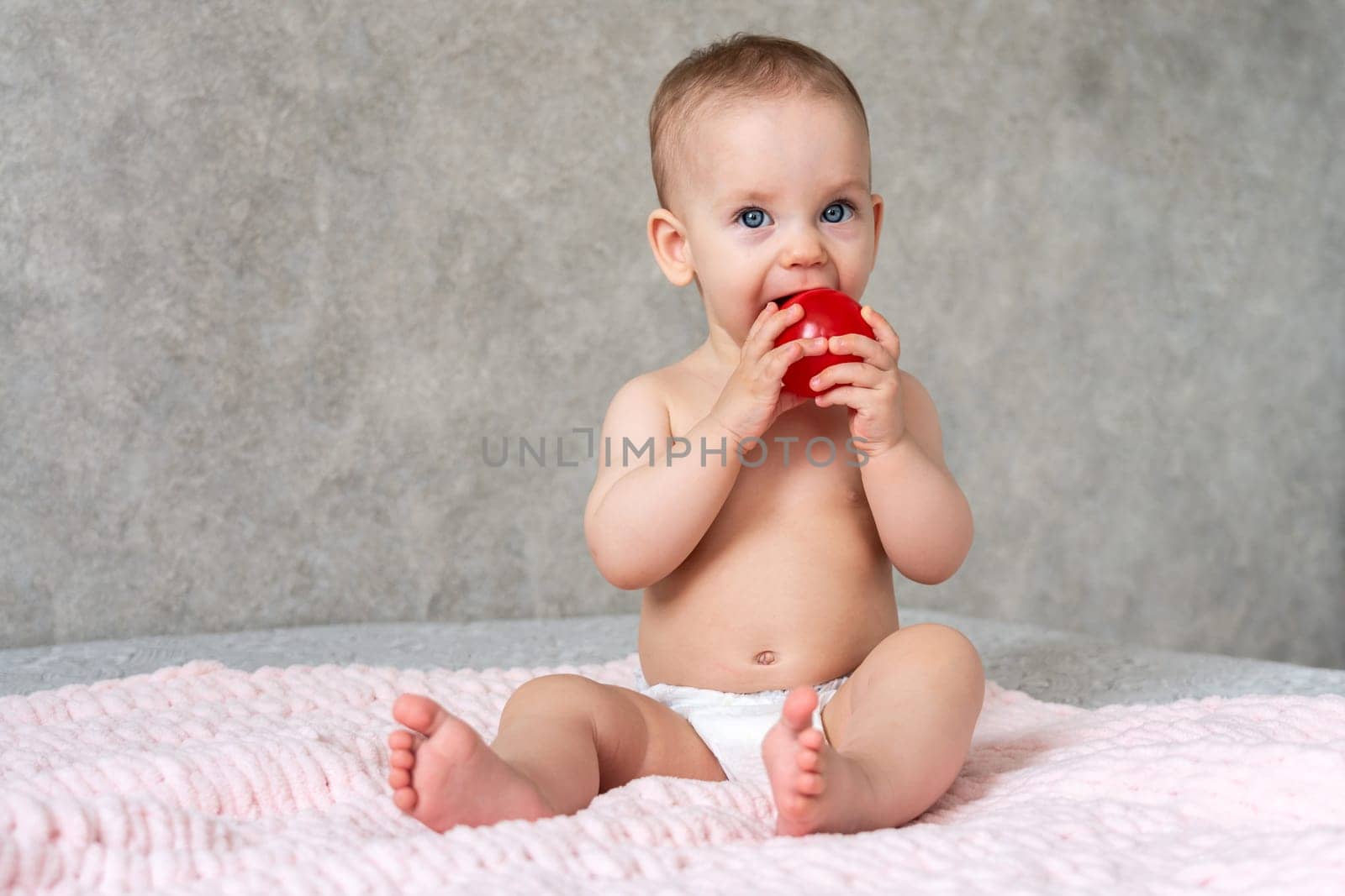 A kid with cheerful eyes is licking a small toy red ball with concentration.