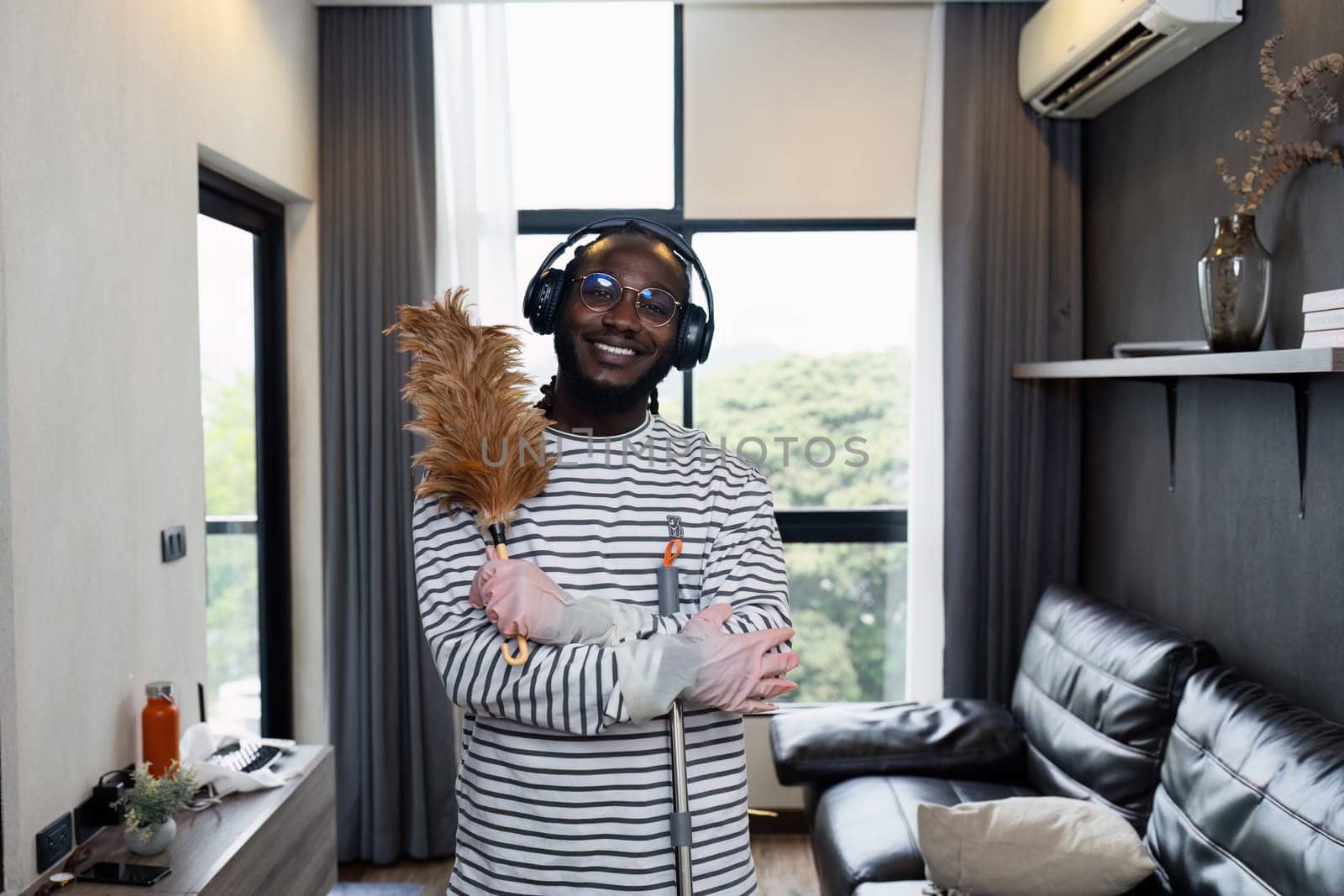 Young African man holding feather cleaning stick for cleaning home and happy looking at camera.