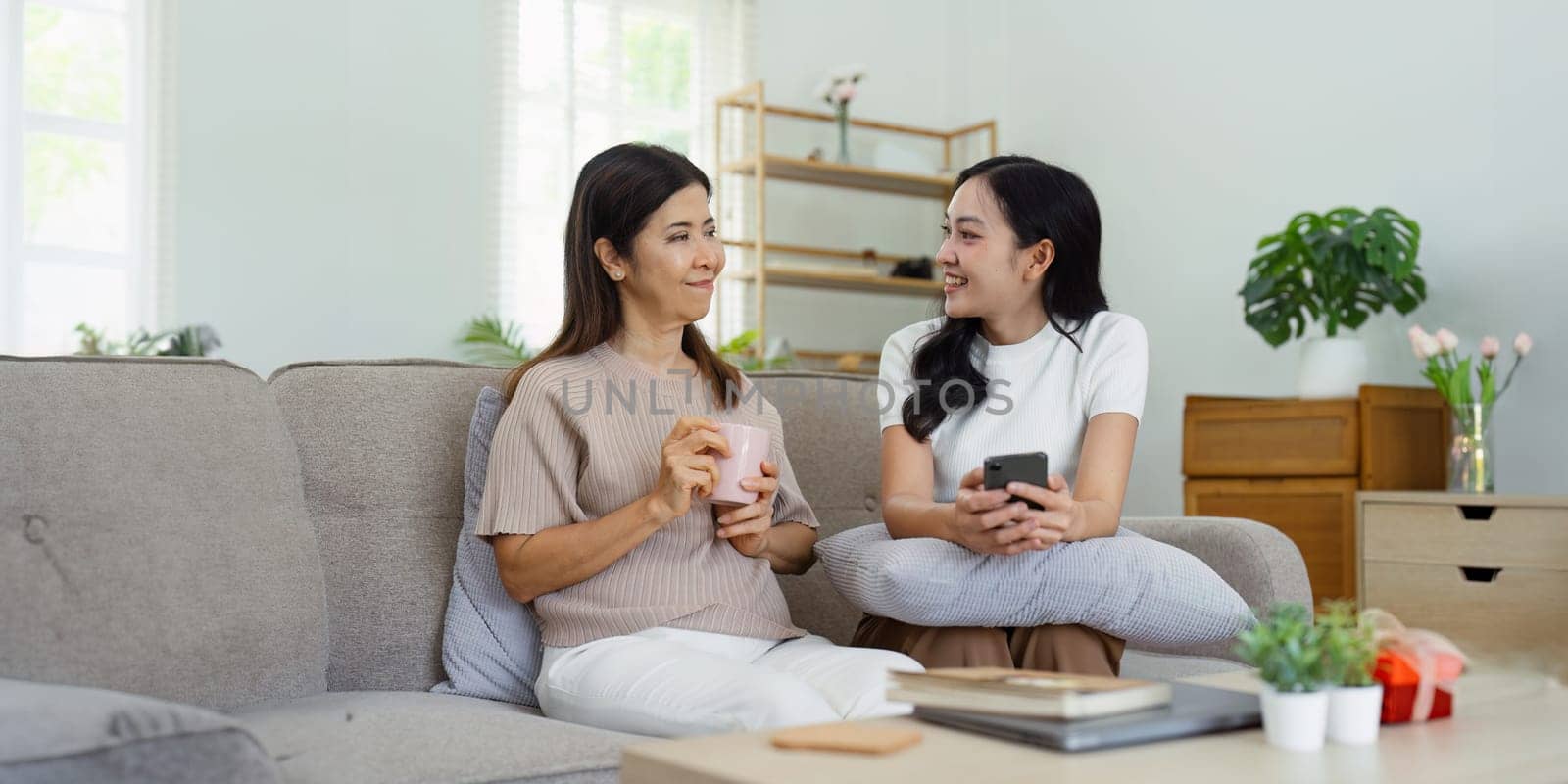 Mother and adult daughter sitting on the sofa together, mother and daughter talking relaxing on weekend together.