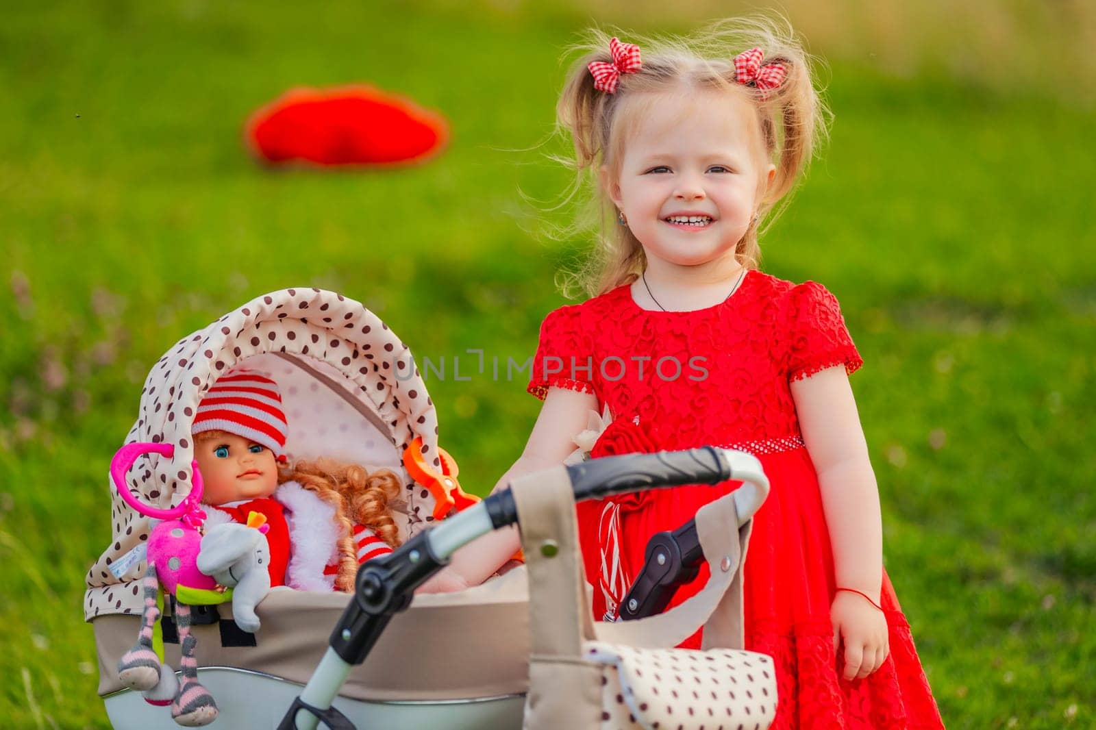 little girl plays with a doll and a stroller on the lawn