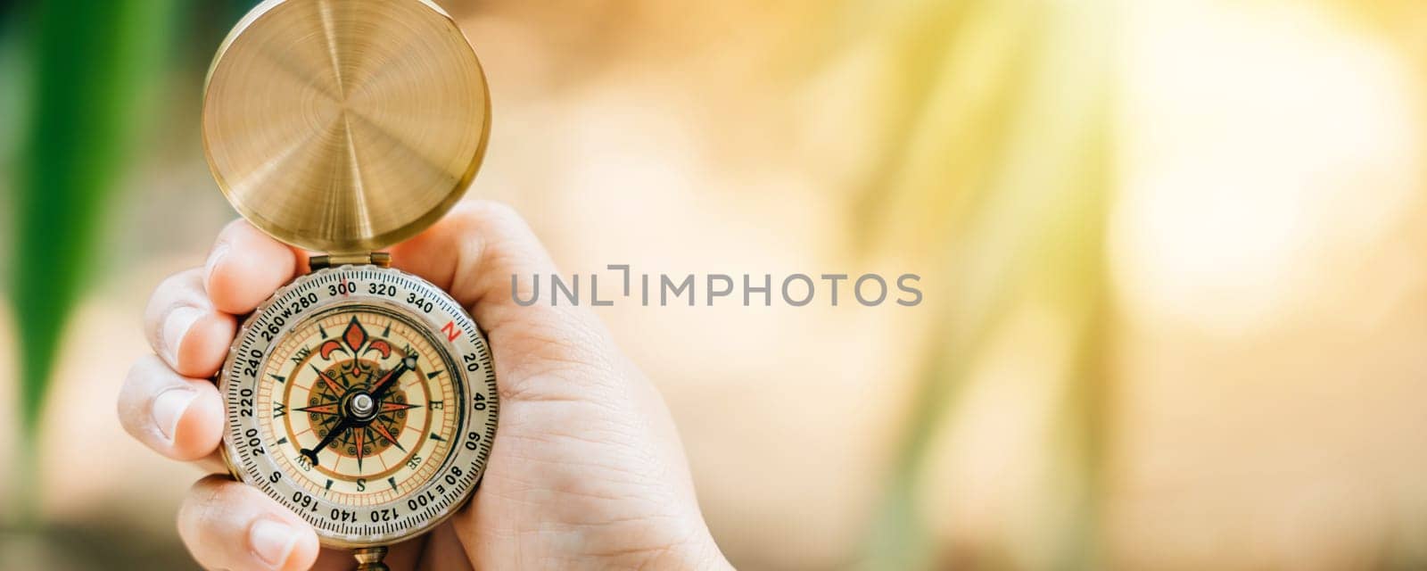 A close-up of a hand grasping a compass in the midst of a lush forest. This image allows for text placement and represents the idea of travel lifestyle and effective business planning and management.