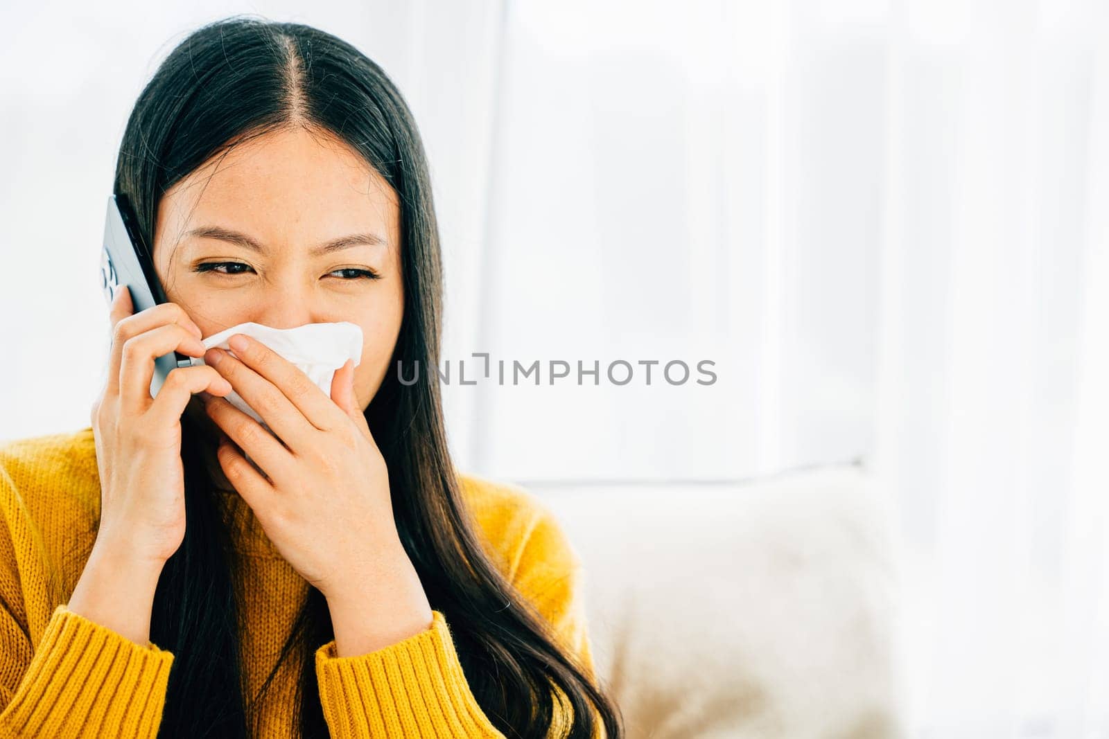 Amidst blowing wiping nose sneezing on sofa a sick female contacts doctor. An ill young girl discusses influenza symptoms with practitioner via phone seeking medicine. Conveying patient care at home.