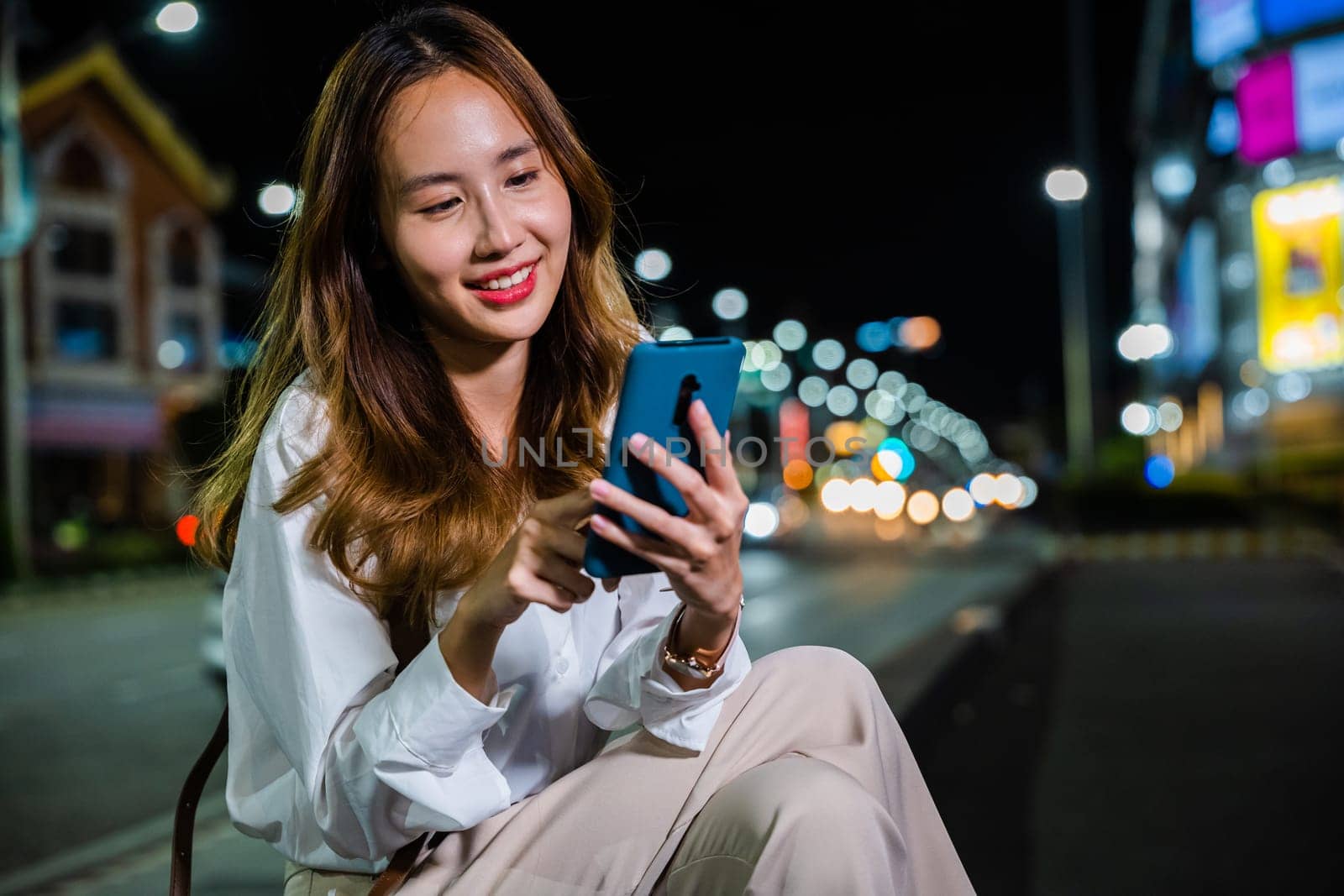 Asian woman's night walk through the city is made efficient with a laptop computer and smartphone by Sorapop