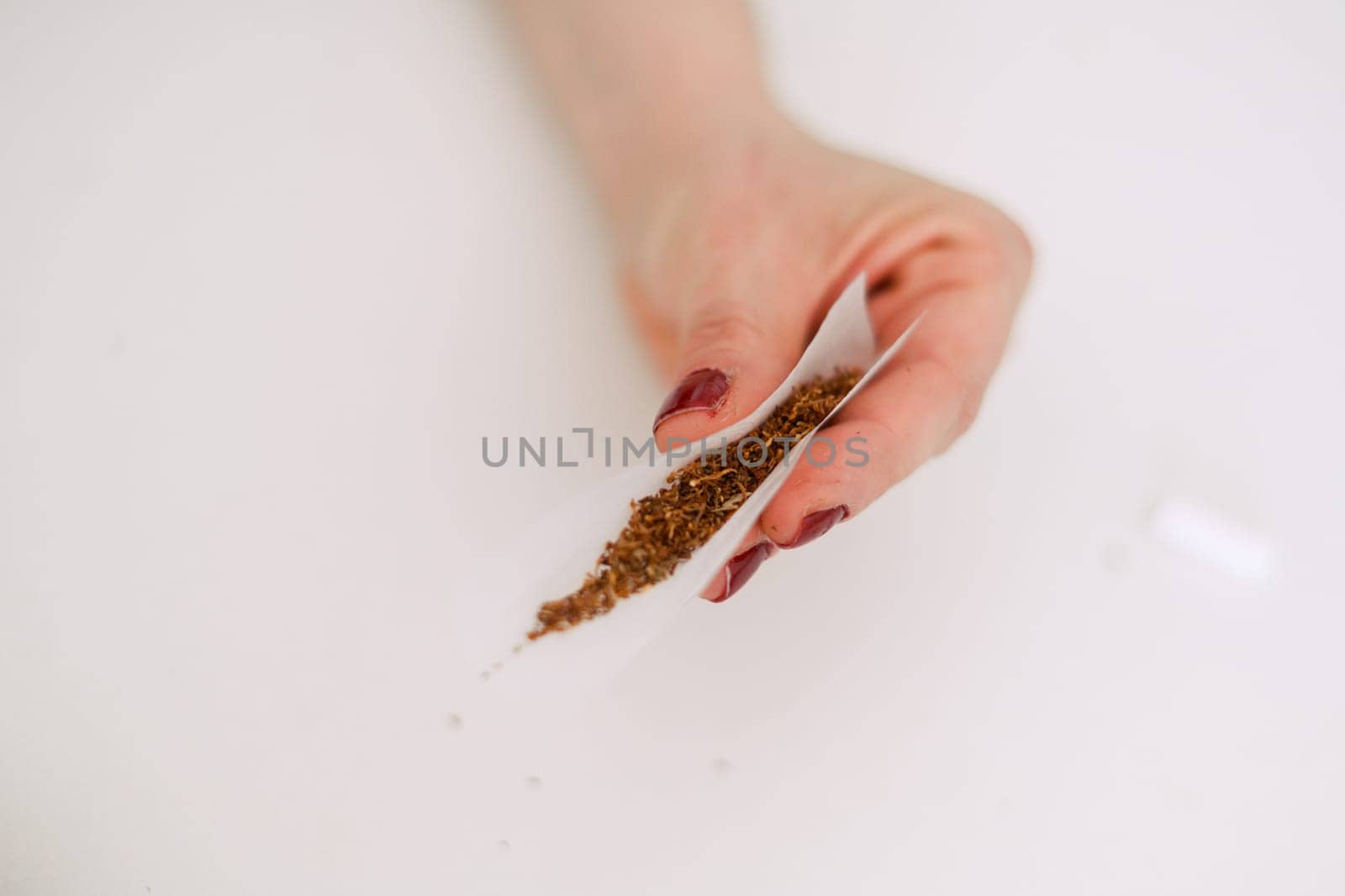 unrecognizable female young adult person prepare smoke hashish tobacco cigarette joint with filter at home on white table for personal health relax use