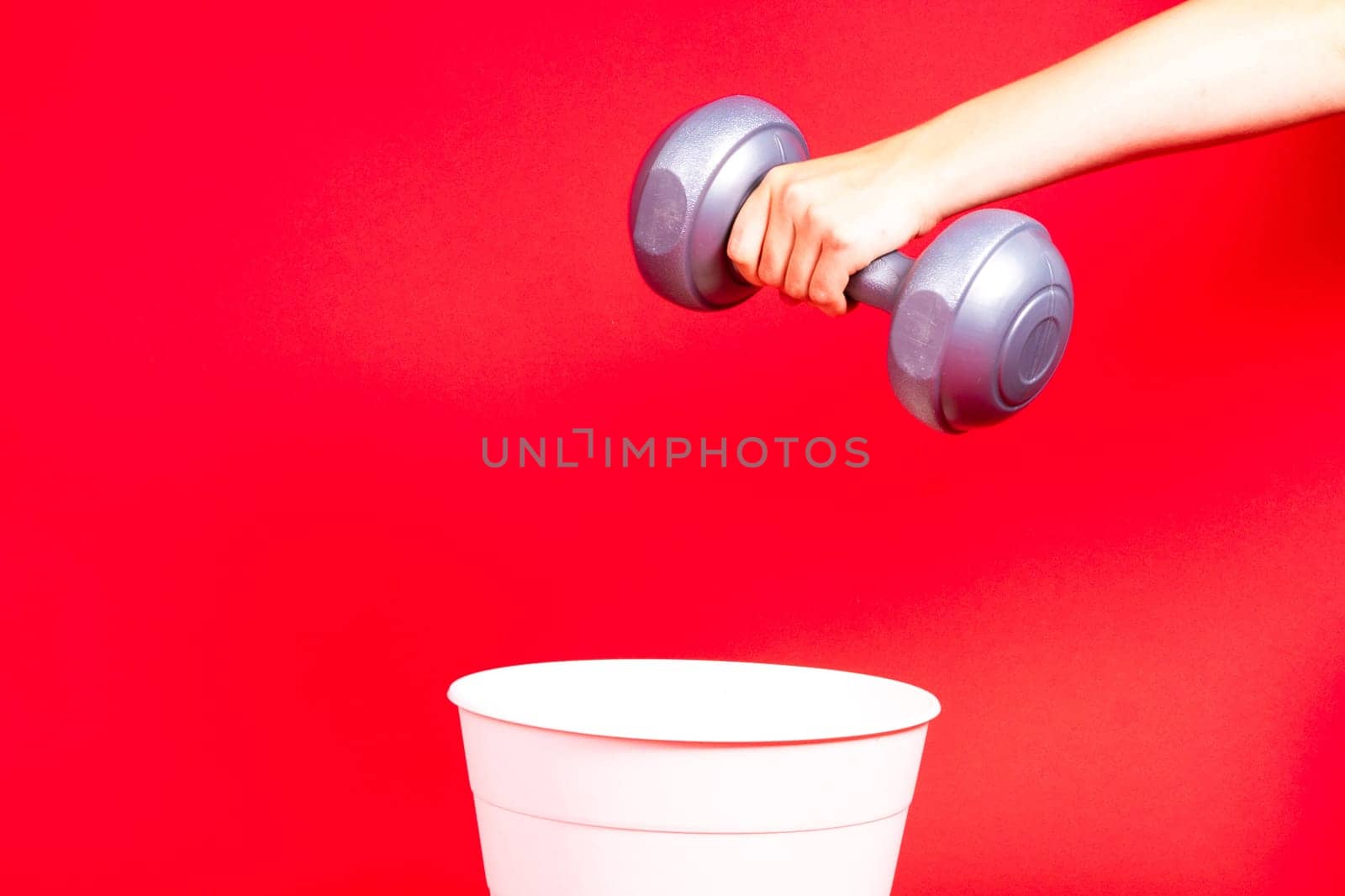 Dumbbells are thrown in the trash can. For copy space for designers on red background