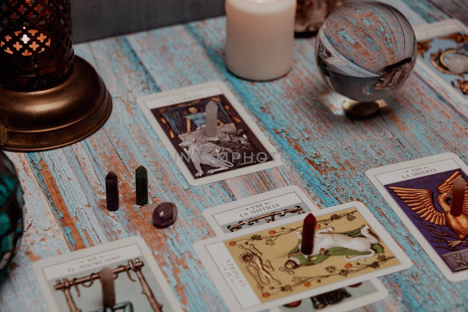 A dimly lit scene showing a spread of tarot cards, alongside crystals, candles, and a crystal ball on a rustic wooden table