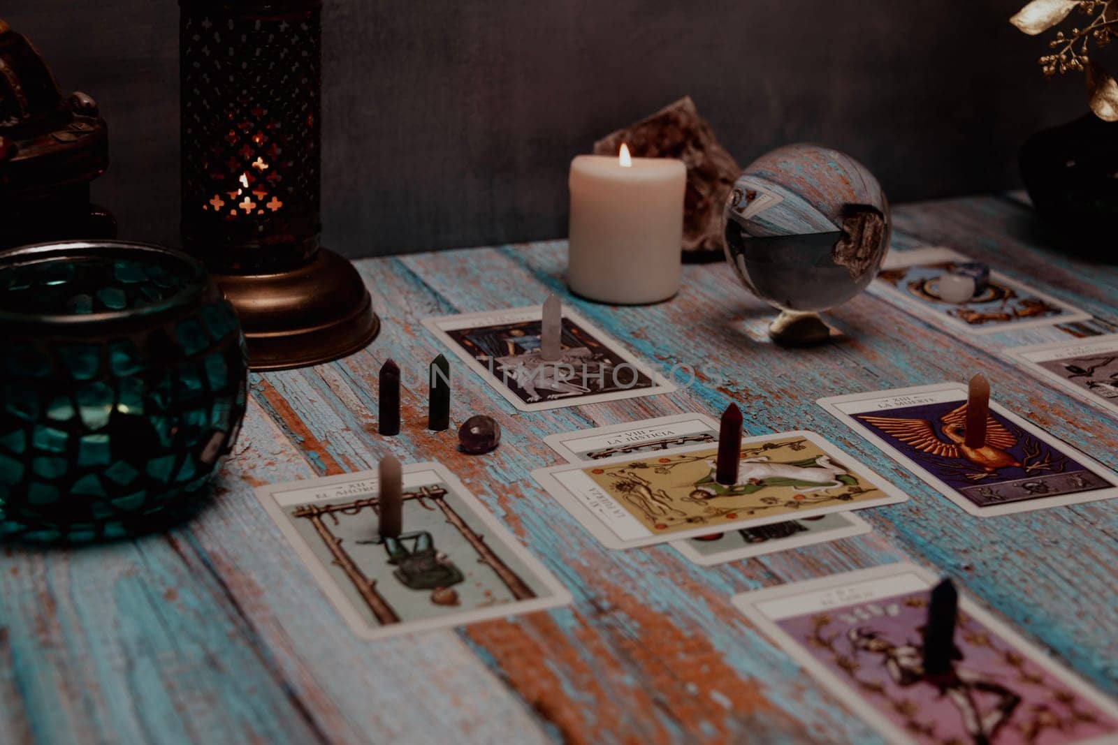 A dimly lit scene showing a spread of tarot cards, alongside crystals, candles, and a crystal ball on a rustic wooden table. by jbruiz78