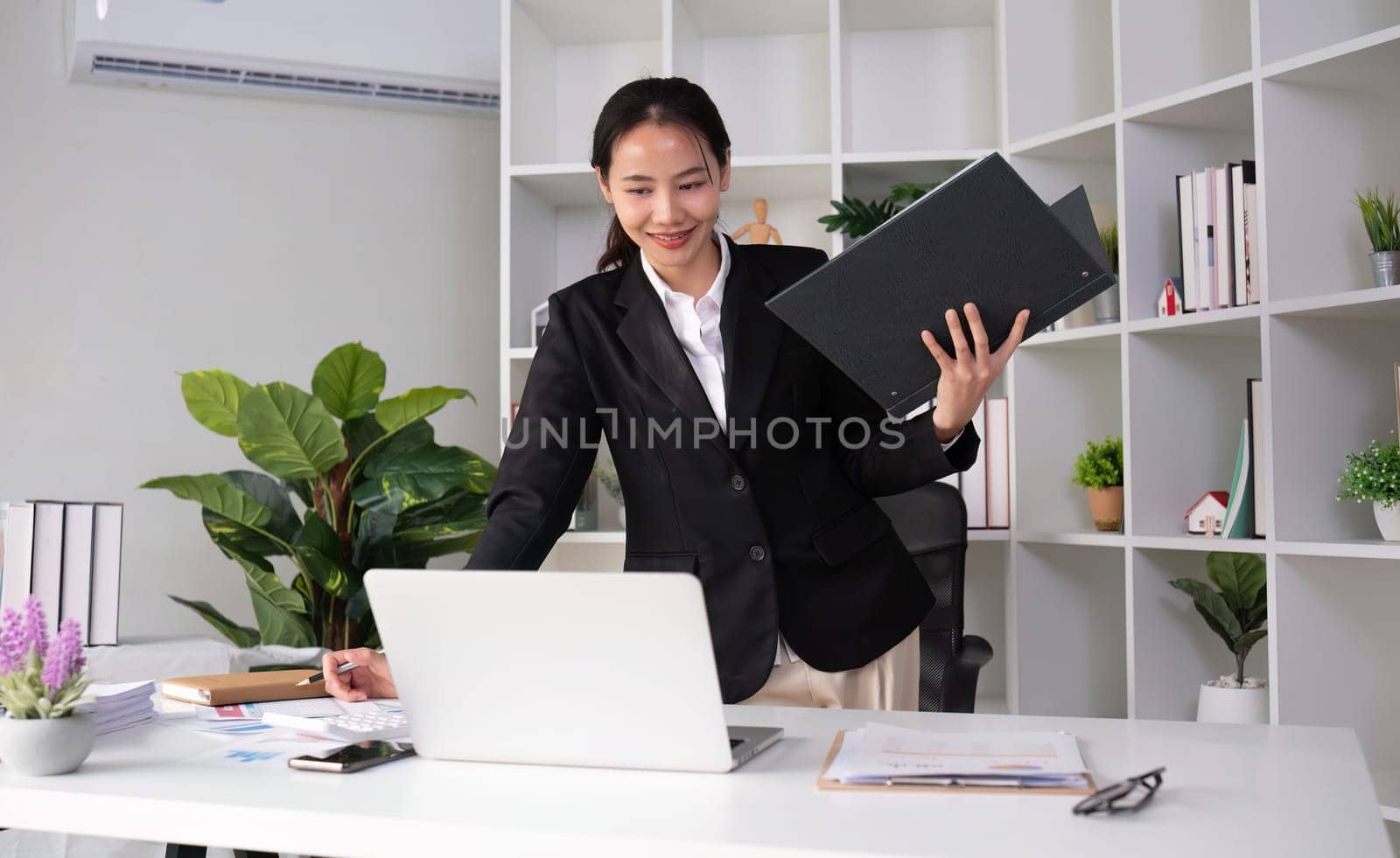 Young Asian business woman in a suit is checking work on her desk in the office..