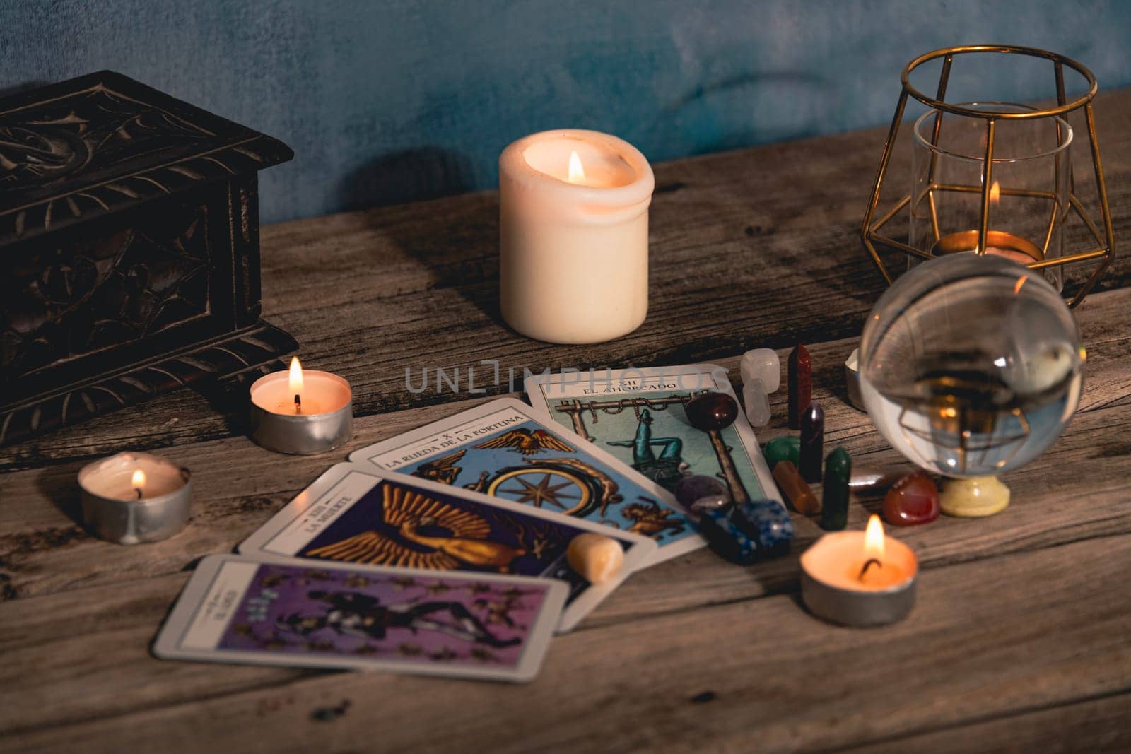 Close-up of a tarot card arrangement with a crystal ball and flickering candles on an aged wooden surface