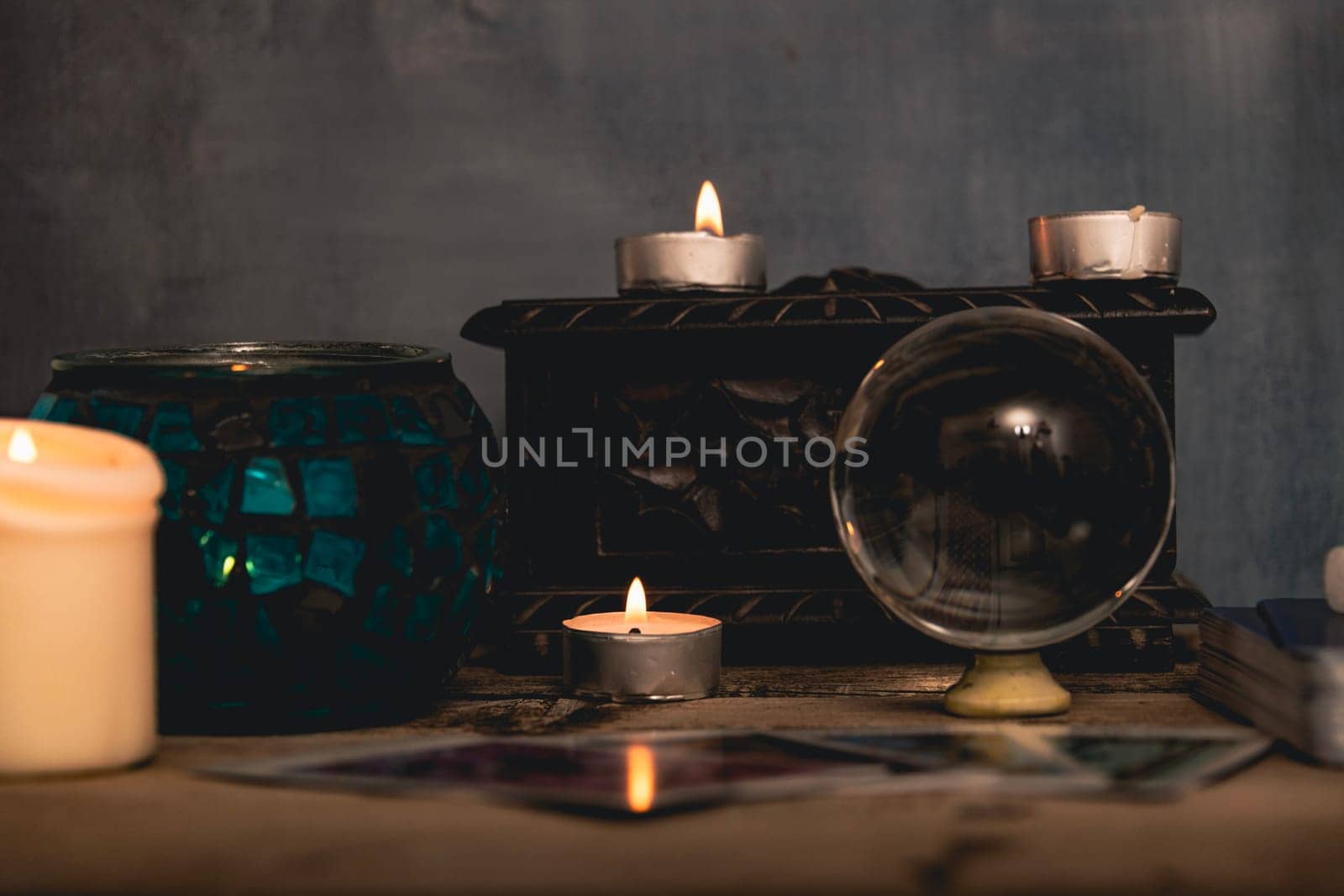 Close-up of a tarot card arrangement with a crystal ball and flickering candles on an aged wooden surface