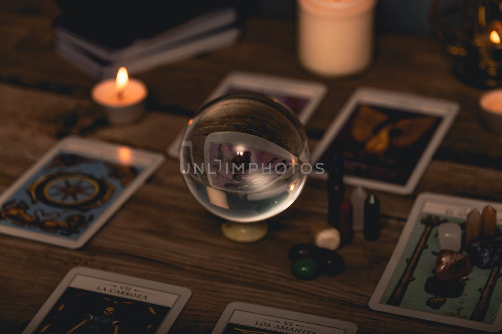 Close-up of a tarot card arrangement with a crystal ball and flickering candles on an aged wooden surface