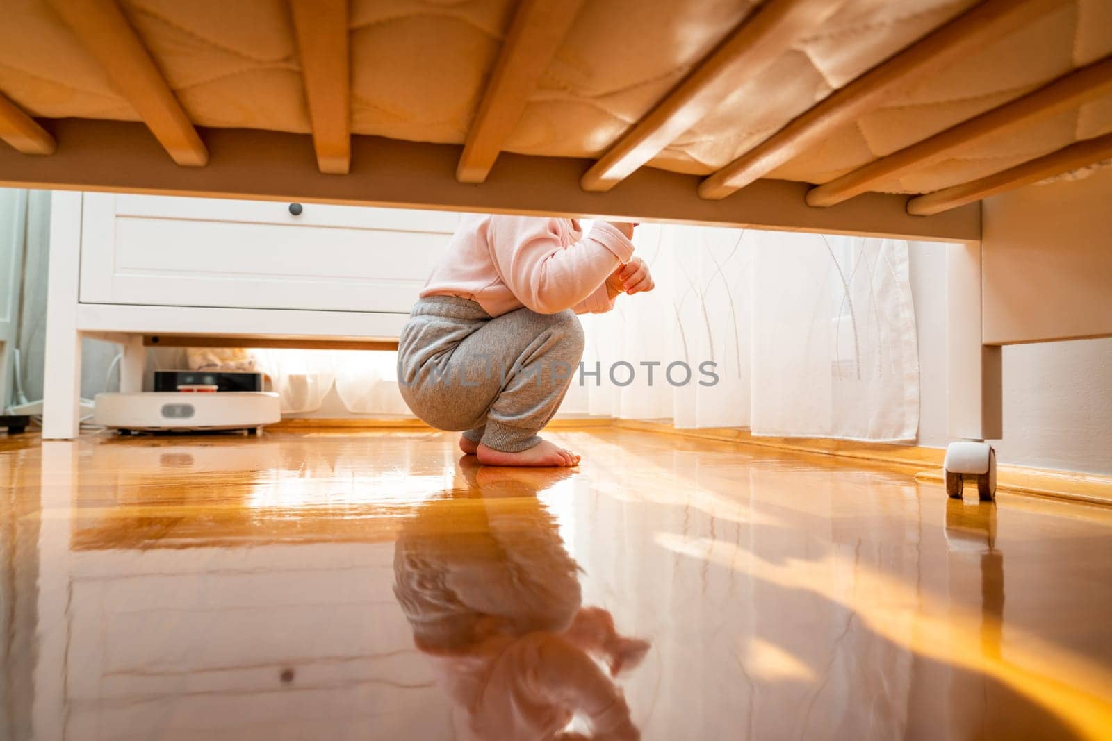 The baby sat down on the parquet floor, photographed from the floor. Hidden frame concept.
