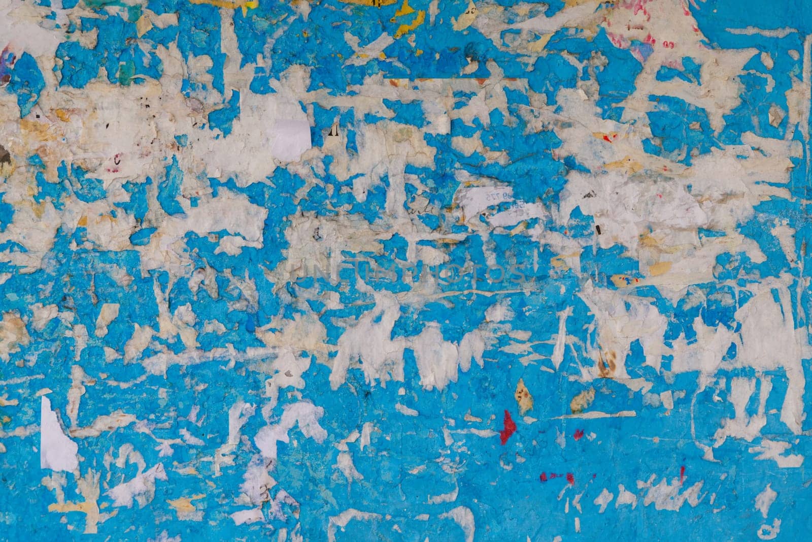 Old wall painted in blue with peeled-off paper advertisements leftovers. Old wall painted yellow with peeled-off paper advertisements leftovers.