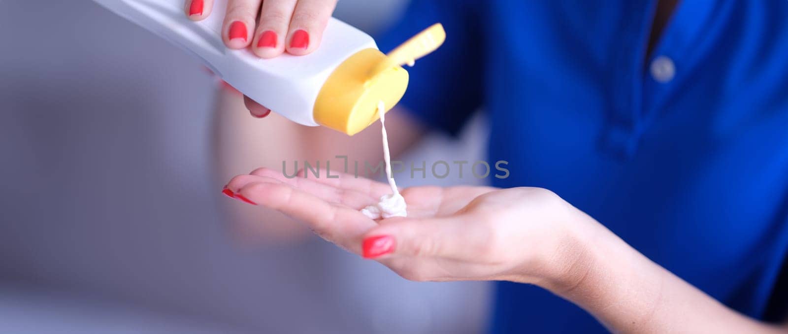 Woman pours body care lotion or sunscreen from bottle into hand. Moisturizing and protecting skin concept